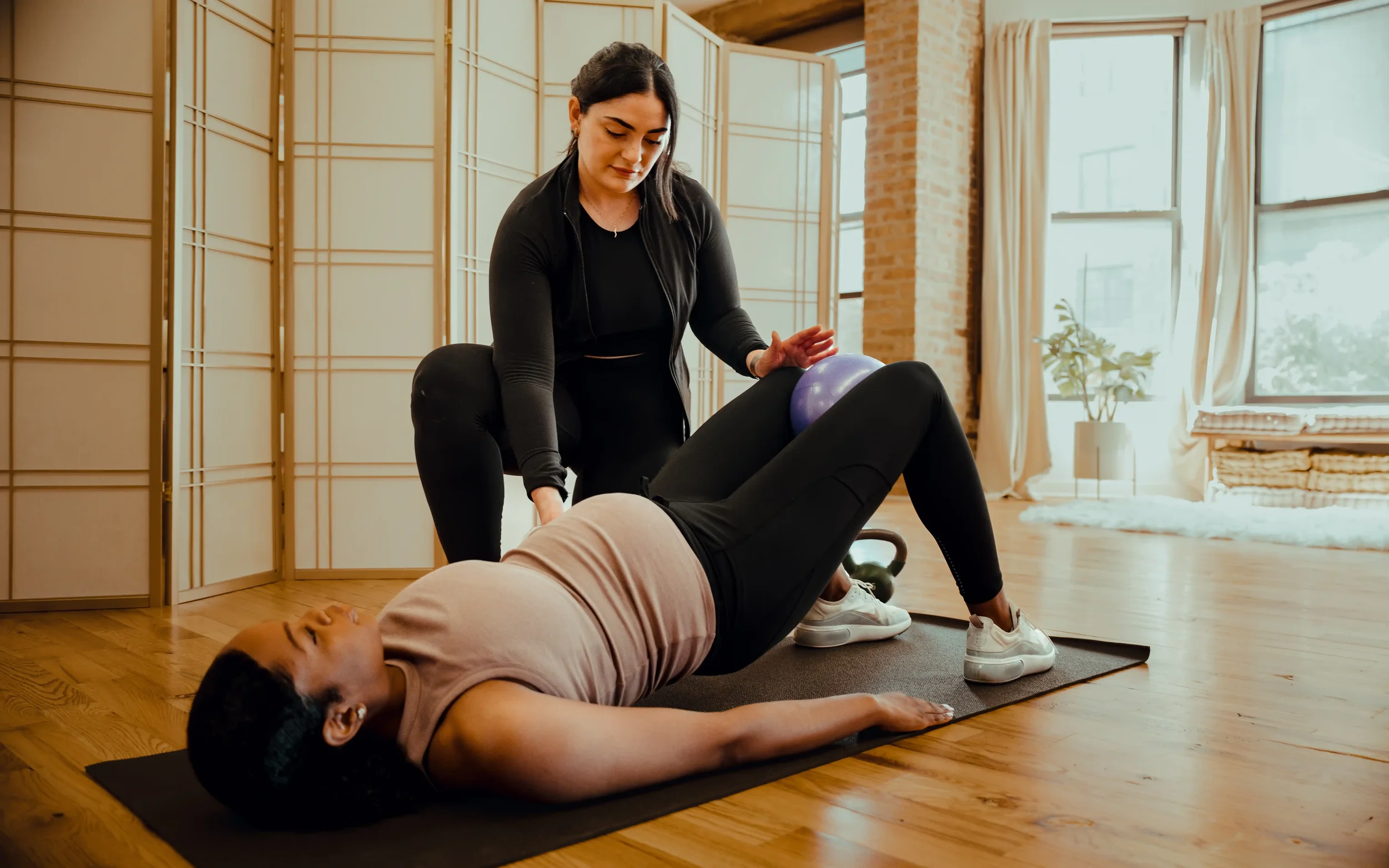 Pregnant woman wearing athleisure doing mat exercises with a physical therapist's guidance.