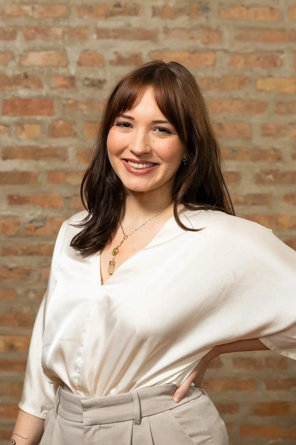 Smiling person with brown hair wearing a black top and a gold necklace.