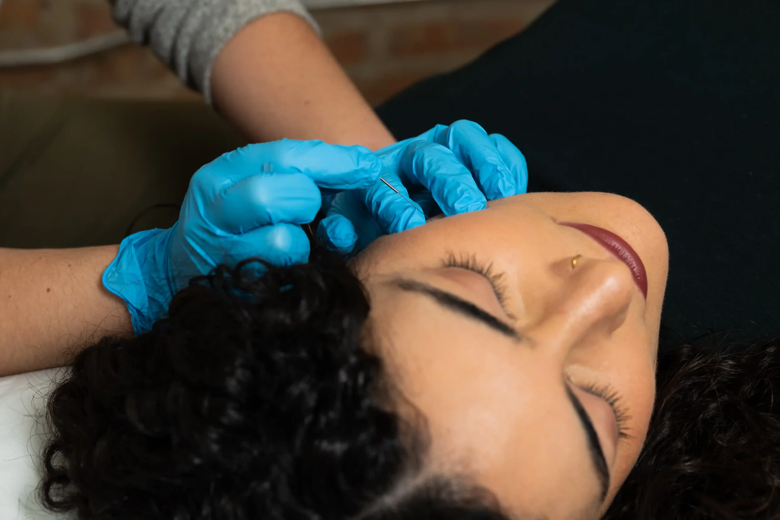 A set of hands wearing plastic gloves holding a small needle up to a patient's jawline.