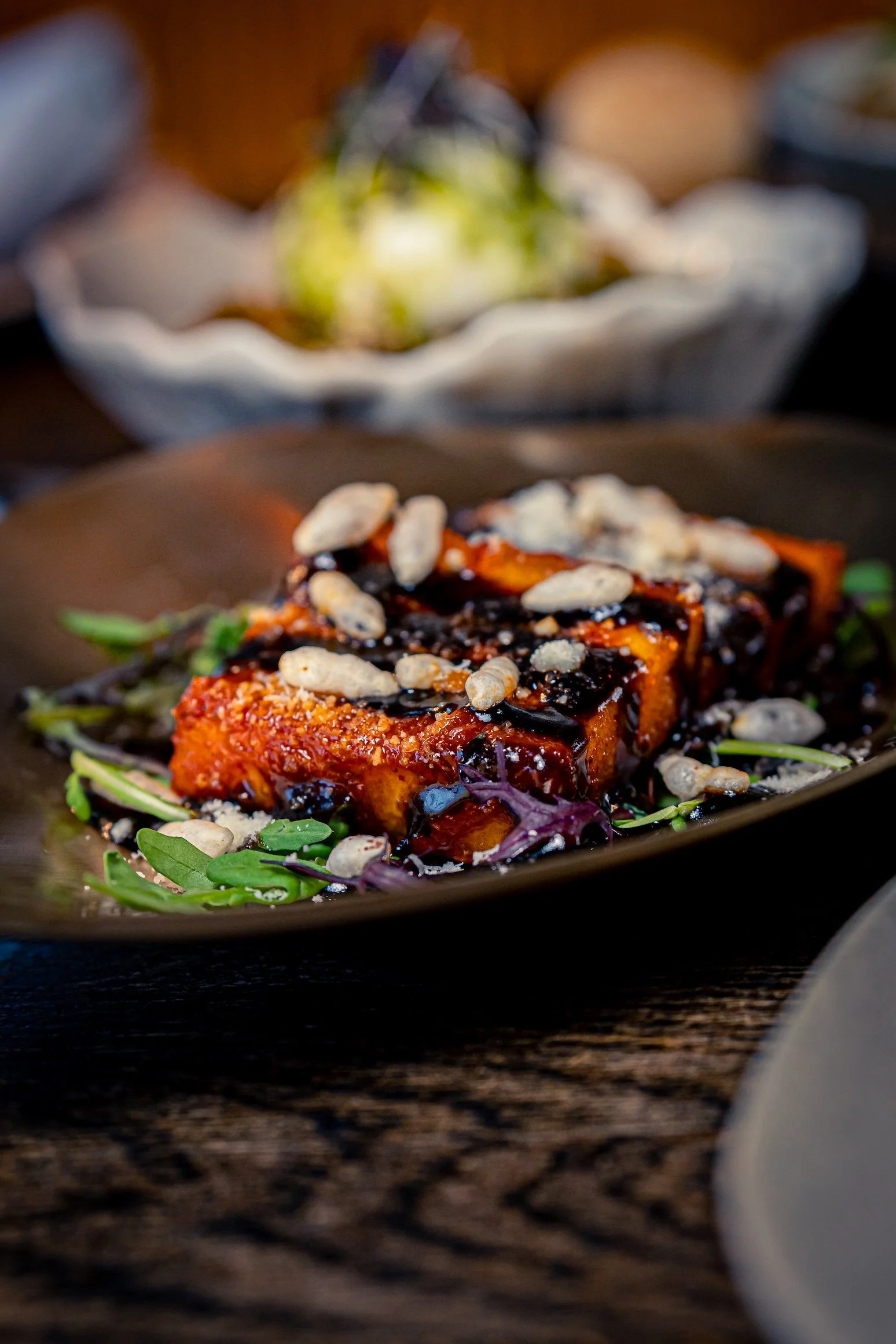 A plated serving of spicy tofu with sauce, garnished with sunflower seeds and greens, on a dark wooden table.