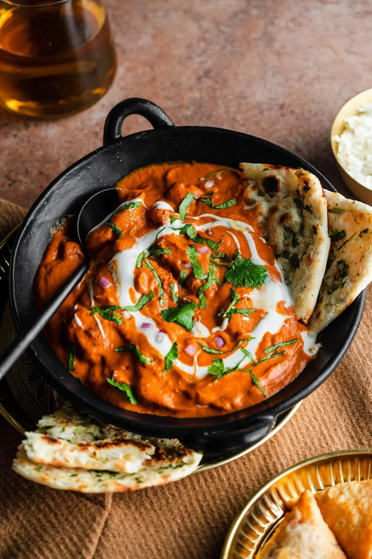 A bowl of Indian butter chicken with naan bread and a side of rice.