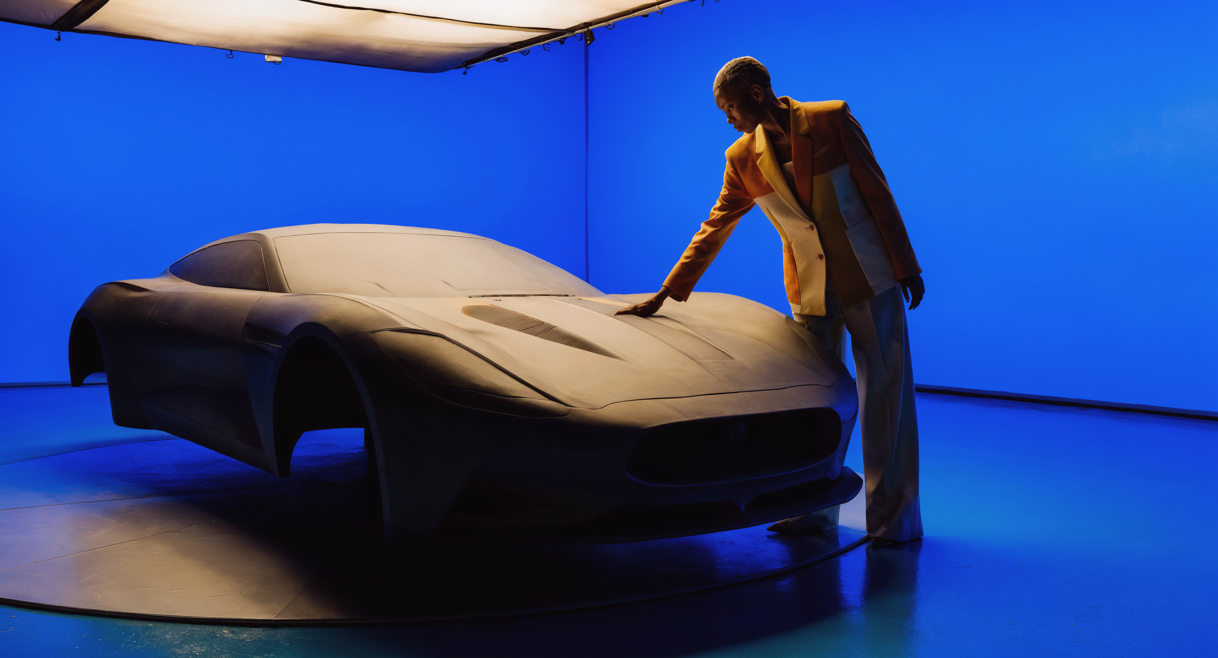 Car_Sculpture_Studio_A_person_in_a_tan_and_orange_blazer_and_white_9dcoBAlx.png