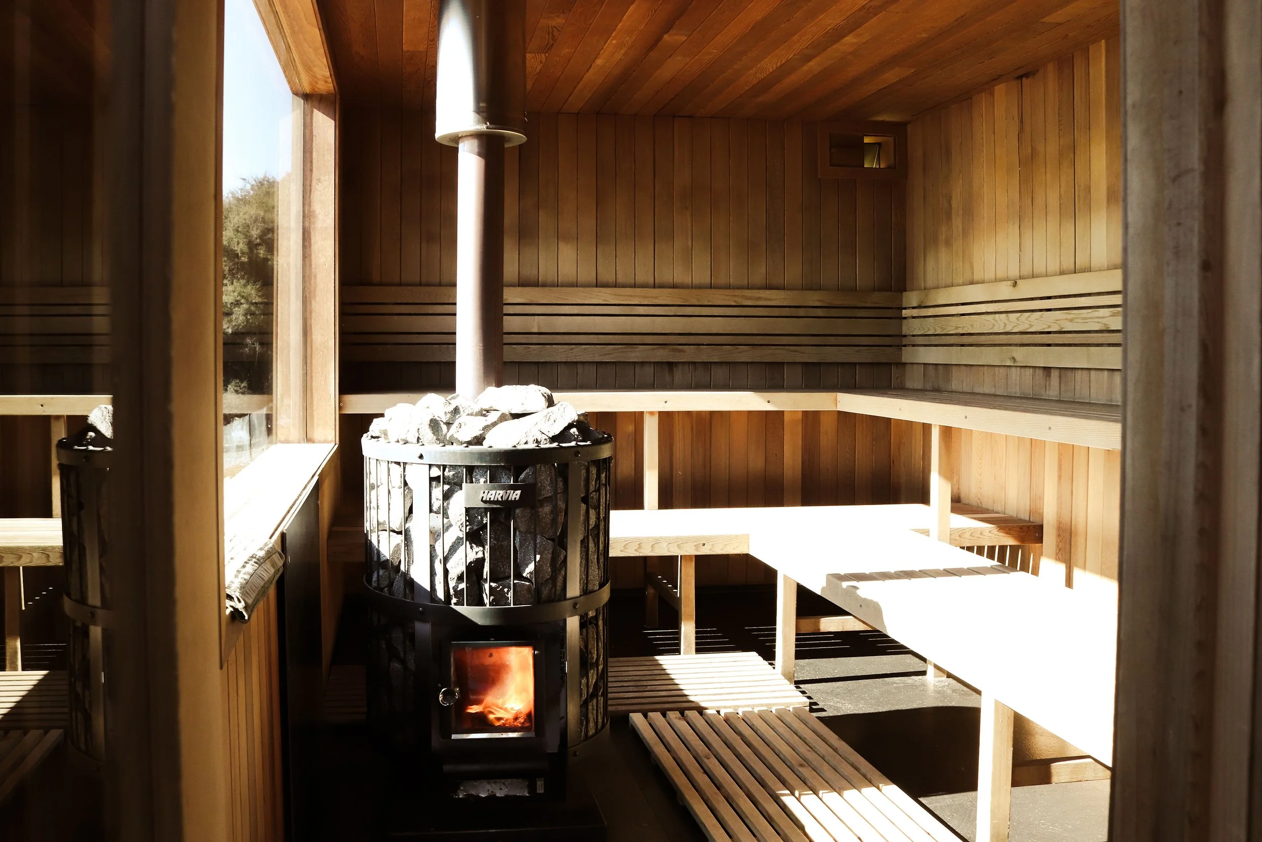 with fire lit  Interior of The Sauna Wānaka, featuring timber benches and a glowing wood-fired stove.