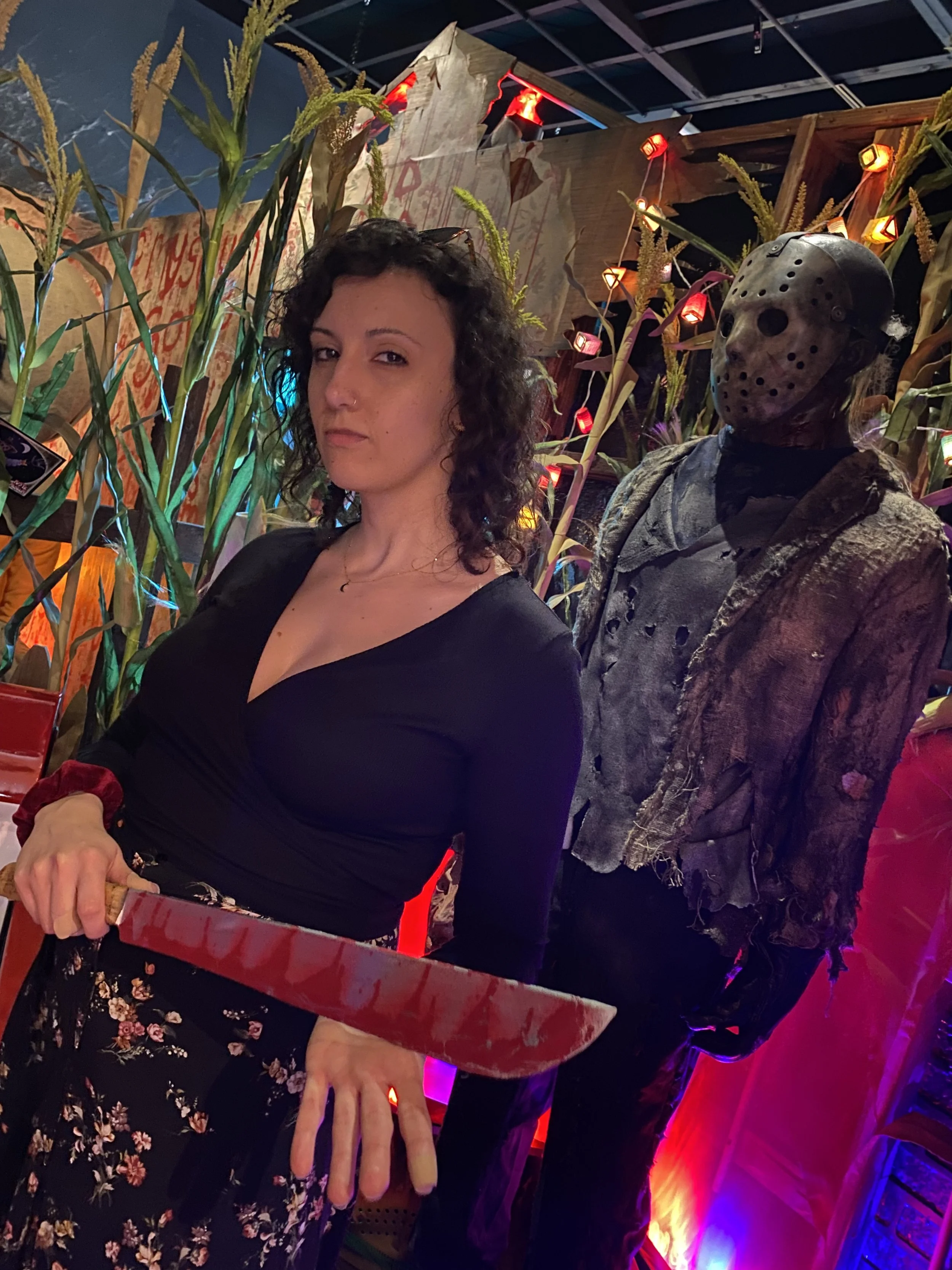 Chelsea with a fake bloody machete in hand posing in front of Jason from the Friday the 13th franchise at the Mystic Museum in Burbank, CA