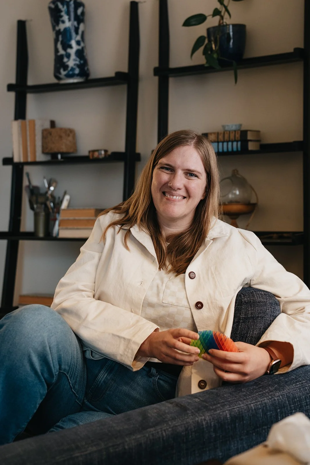 Kristin sits in her therapy office chair. She holds a stim tool and smiles at the camera.
