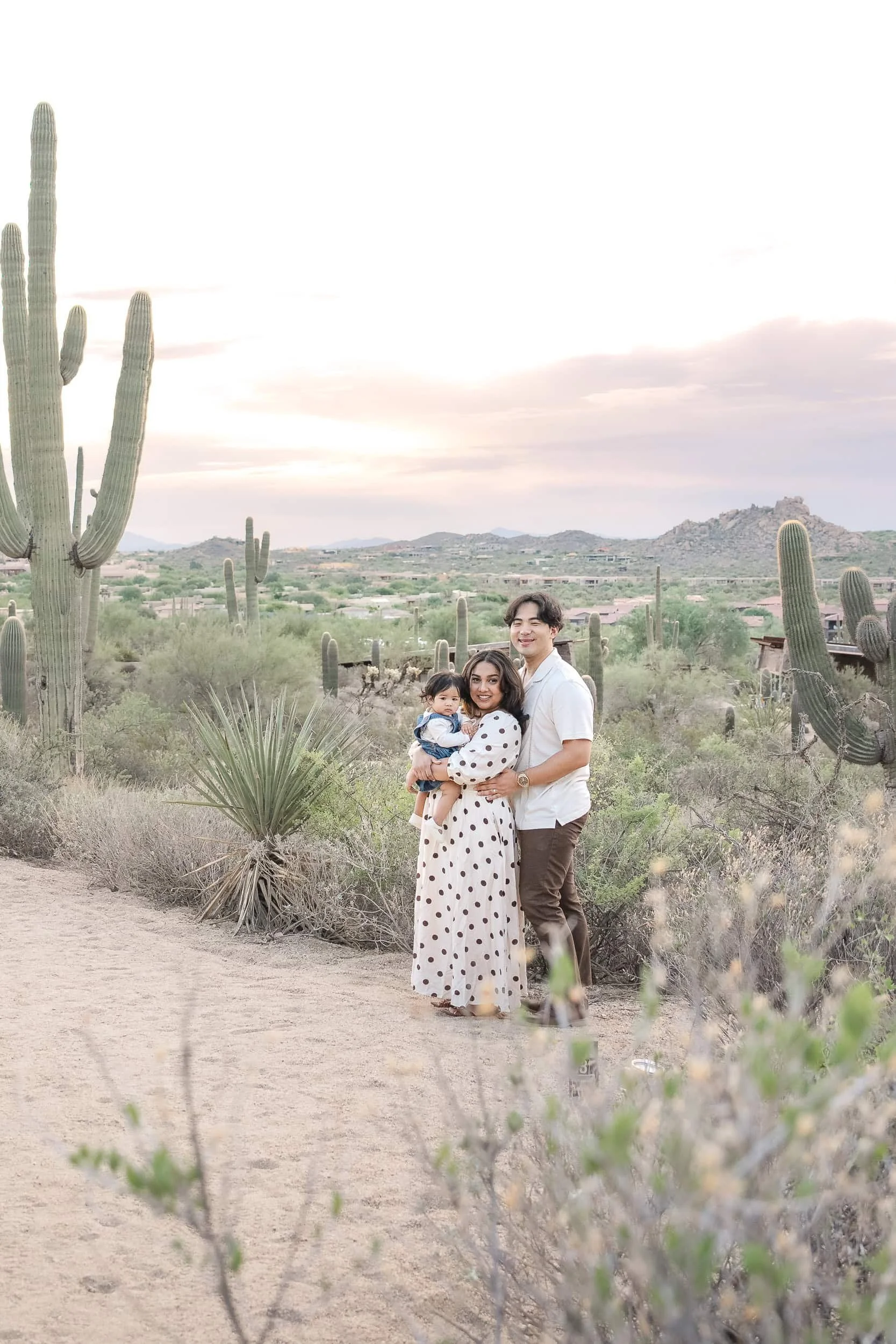 mom and dad posing for family photos with a young baby in the Arizona desert