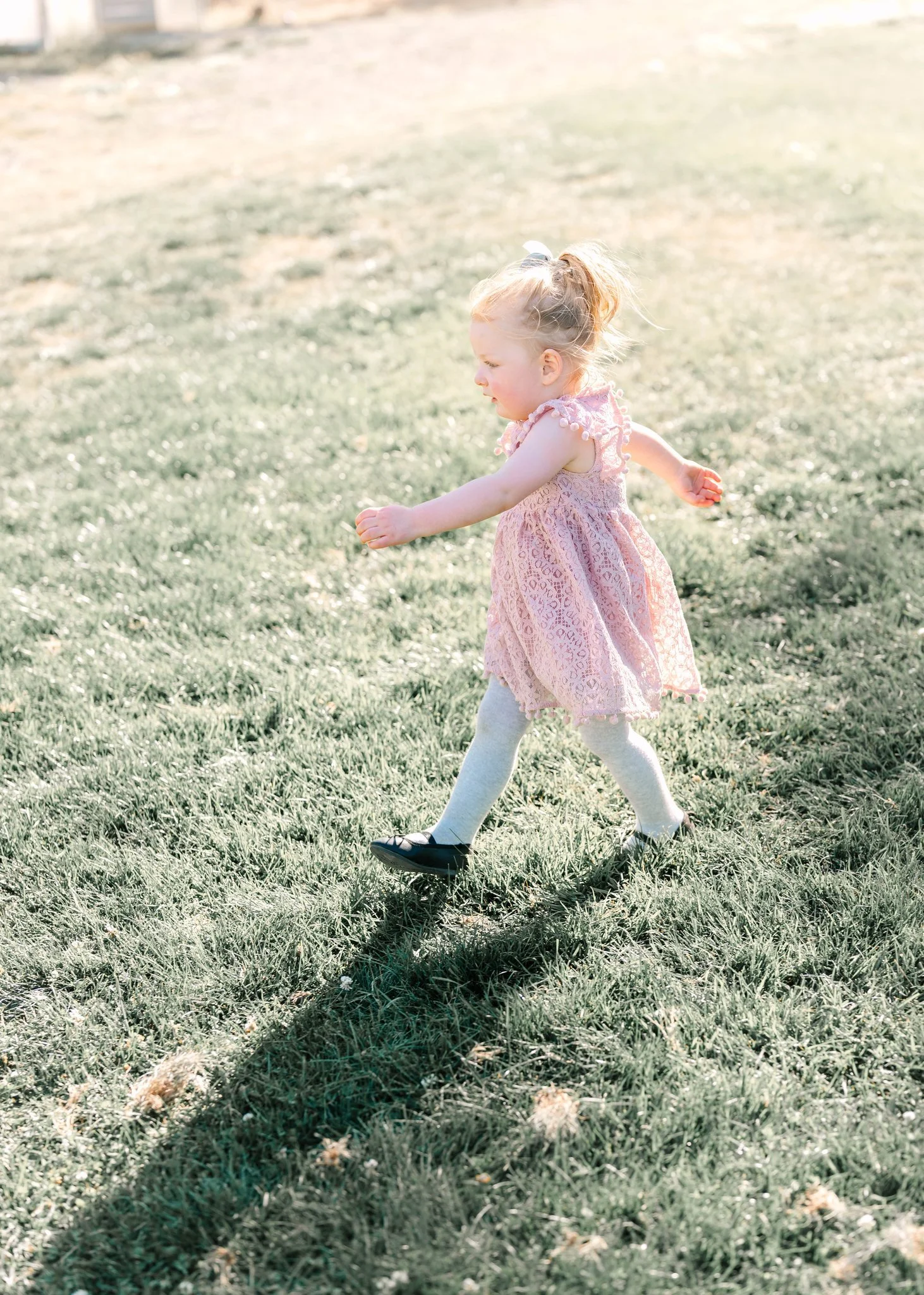 candid photo of a little girl in a pink lace dress walking fast