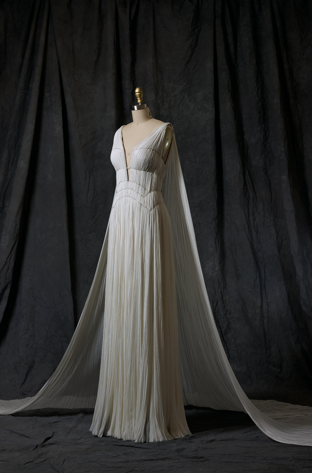 Elegant white pleated gown displayed on a mannequin against a dark backdrop.