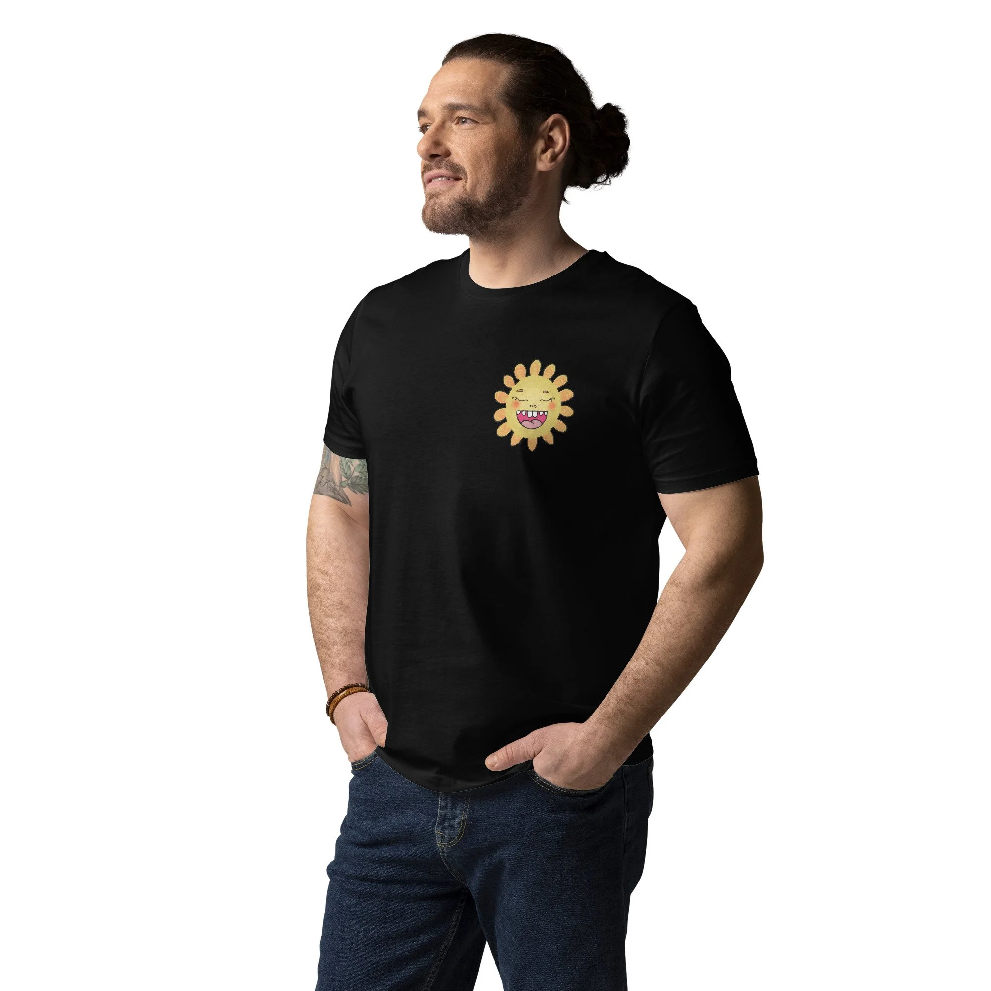 Man with long hair pulled back, beard, and tattoo on arm wearing Pedestrian brand black t-shirt with a colorful smiling sun cartoon graphic on chest and blue jeans, standing with hands in pockets.