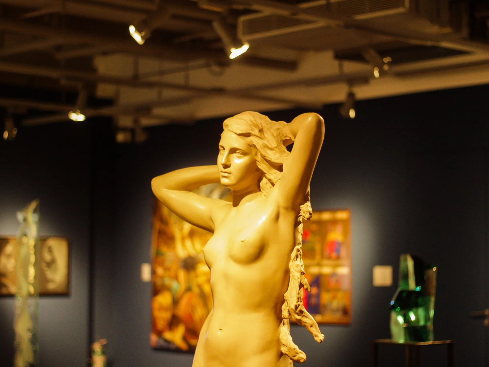 A sculpture of a woman with her arms raised behind her head, displayed in an art gallery.