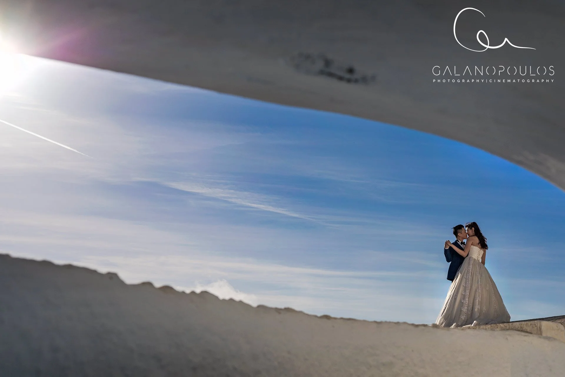 Santorini wedding photography editorial cliffside shot on the Fira caldera edge showcasing a flowing gown, layered caldera cliffs and deep blue Aegean sea.