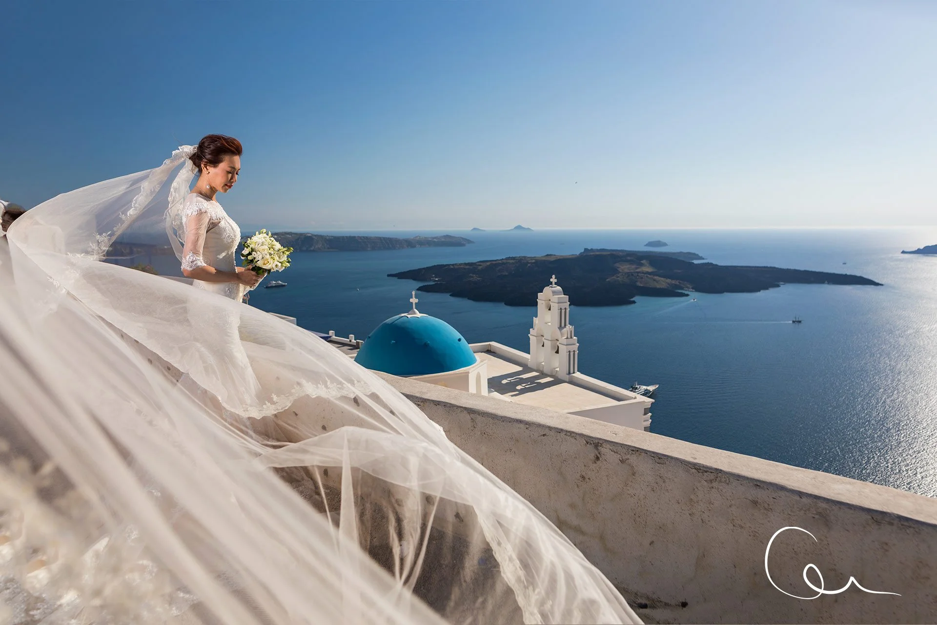 Santorini wedding photography bride portrait at Oia blue domes at sunrise with pastel sky, iconic Cycladic architecture and Aegean sea in the background.