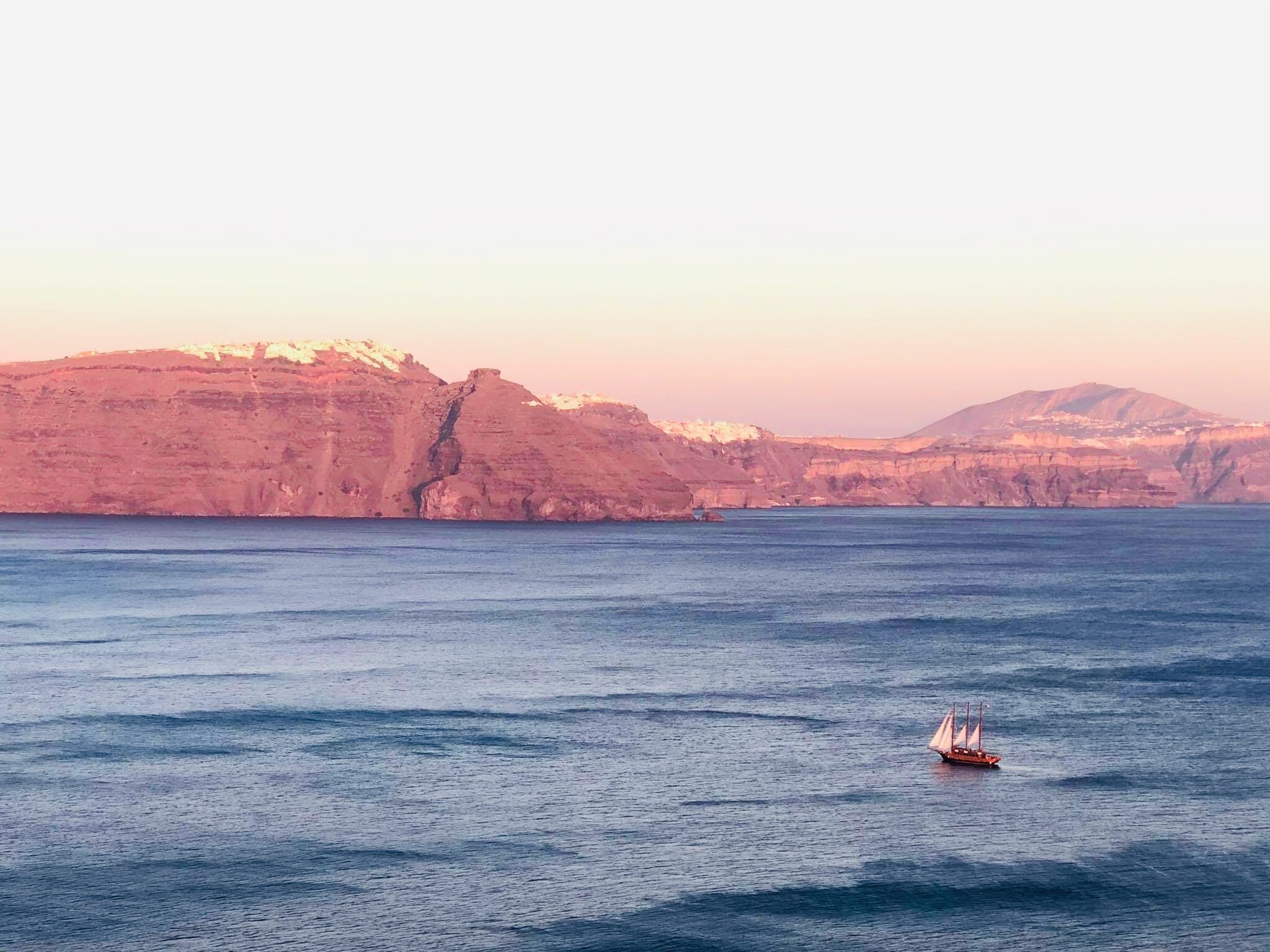 Sunset catamaran cruise with passengers enjoying BBQ and caldera views — Santorini boat tour comparison and booking tip. 黃昏雙體船巡航與甲板燒烤 — Santorini 船遊比較與預訂建議。