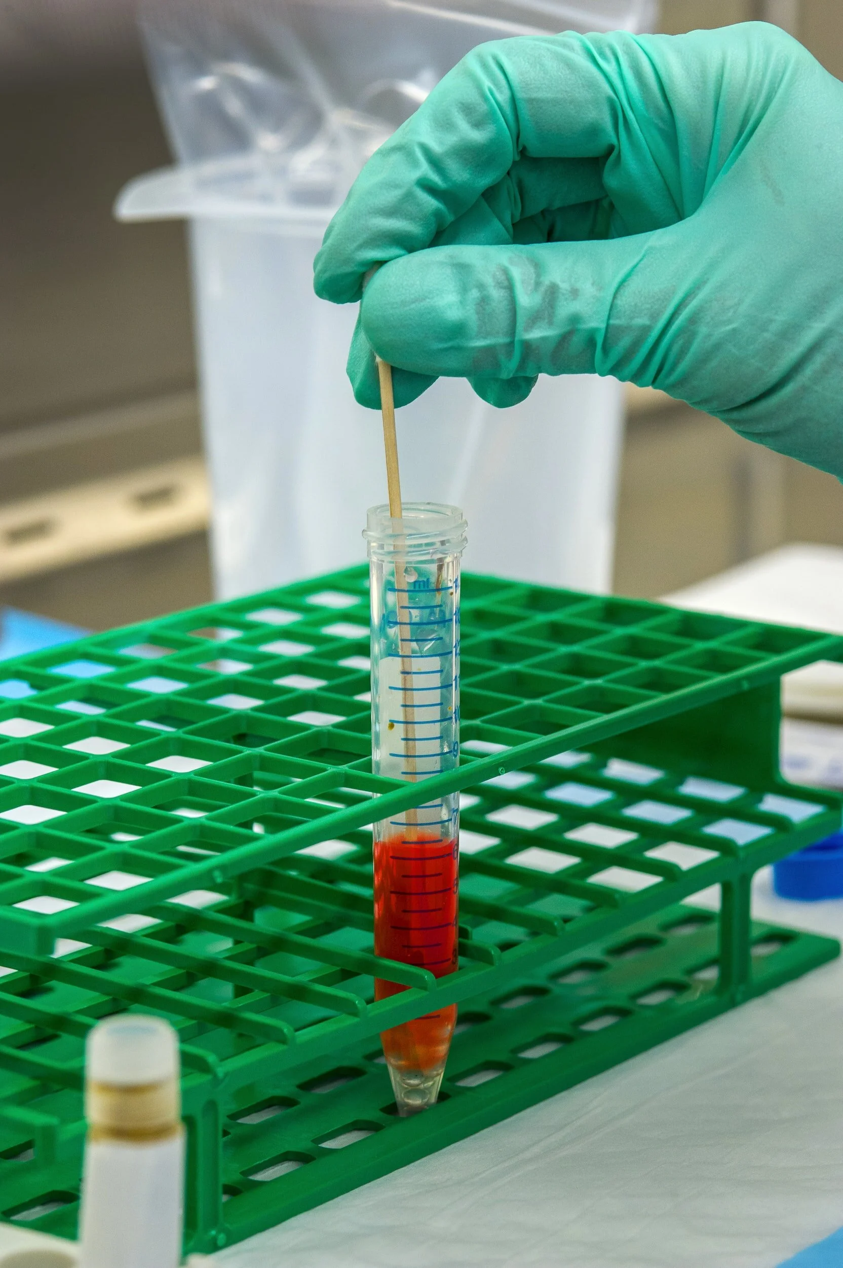A scientist in green gloves handling a test tube with blood in a laboratory setting.