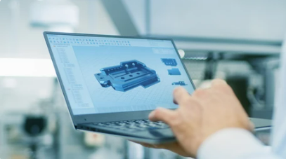 Person holding a laptop displaying a 3D CAD model of a mechanical part in a modern industrial setting.