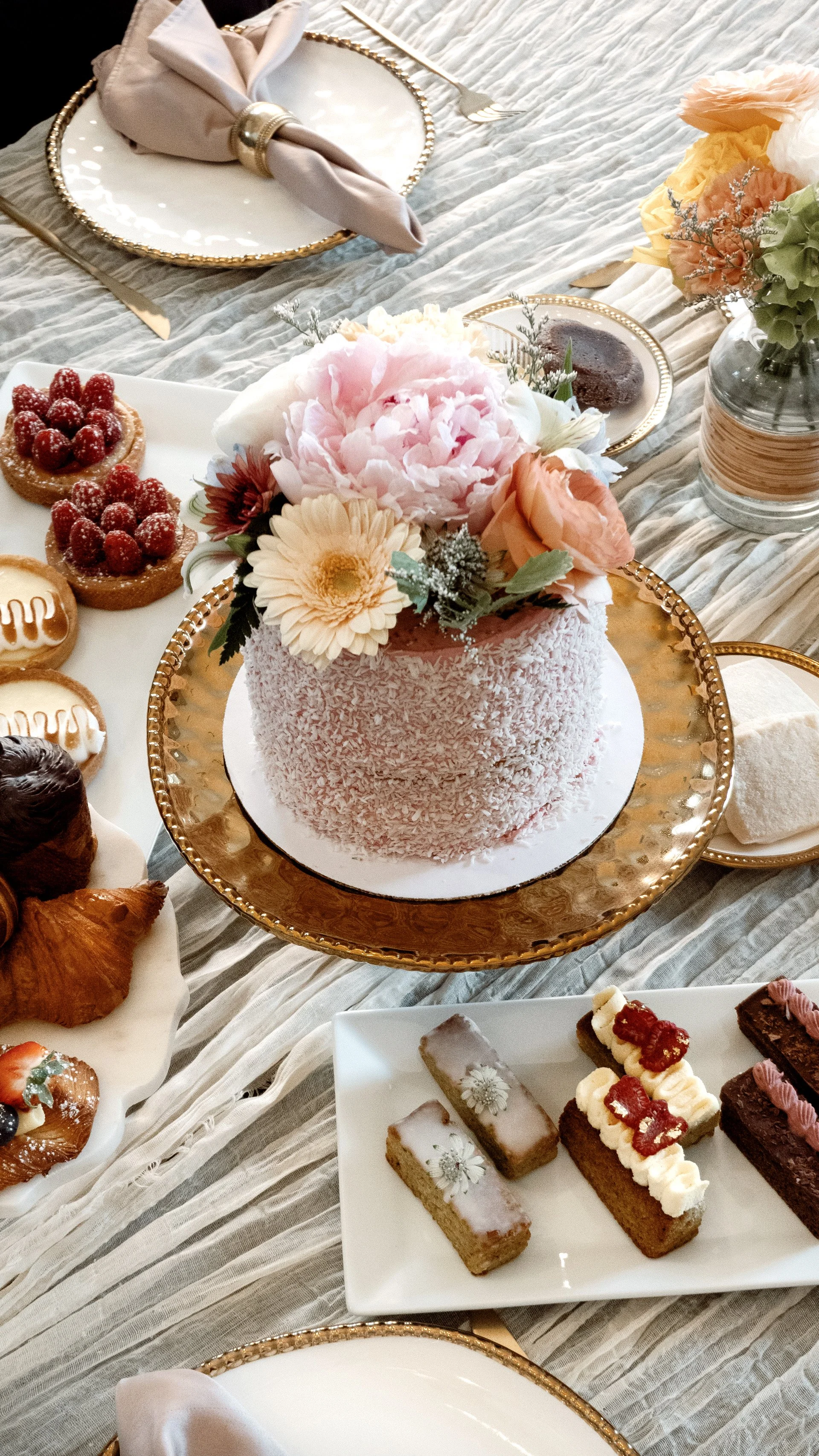 Coconut cake with florals on cake stand with tartes and financiers.