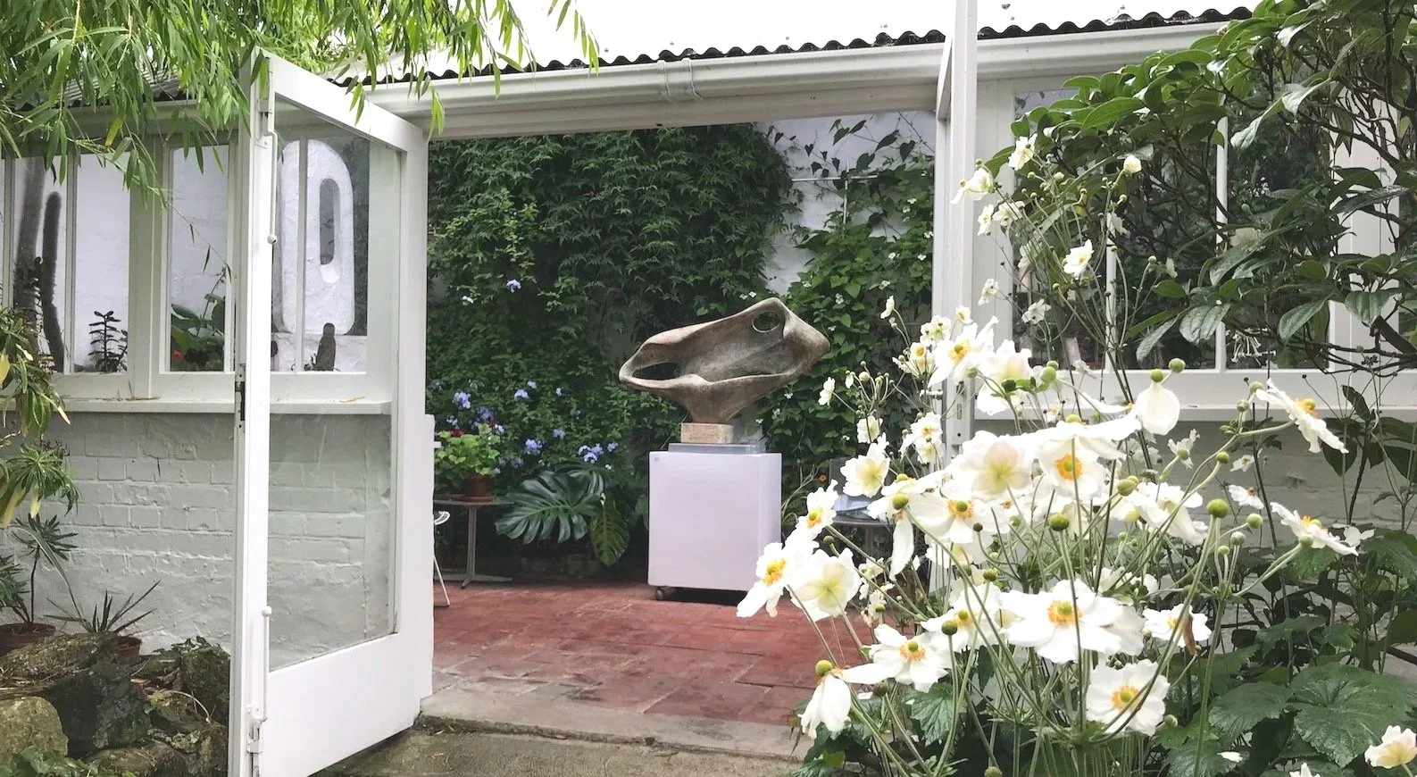 Barbara Hepworth's greenhouse in St Ives with Japanese anemones in the foreground and the sculpture Porthmeor in the background