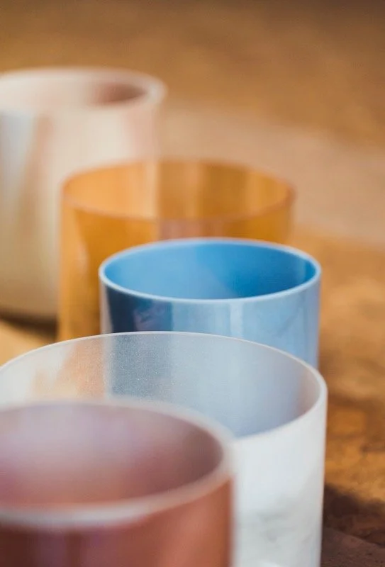 An arrangement of Crystal Tones singing bowls in a line on a wooden surface, with a blurred background.