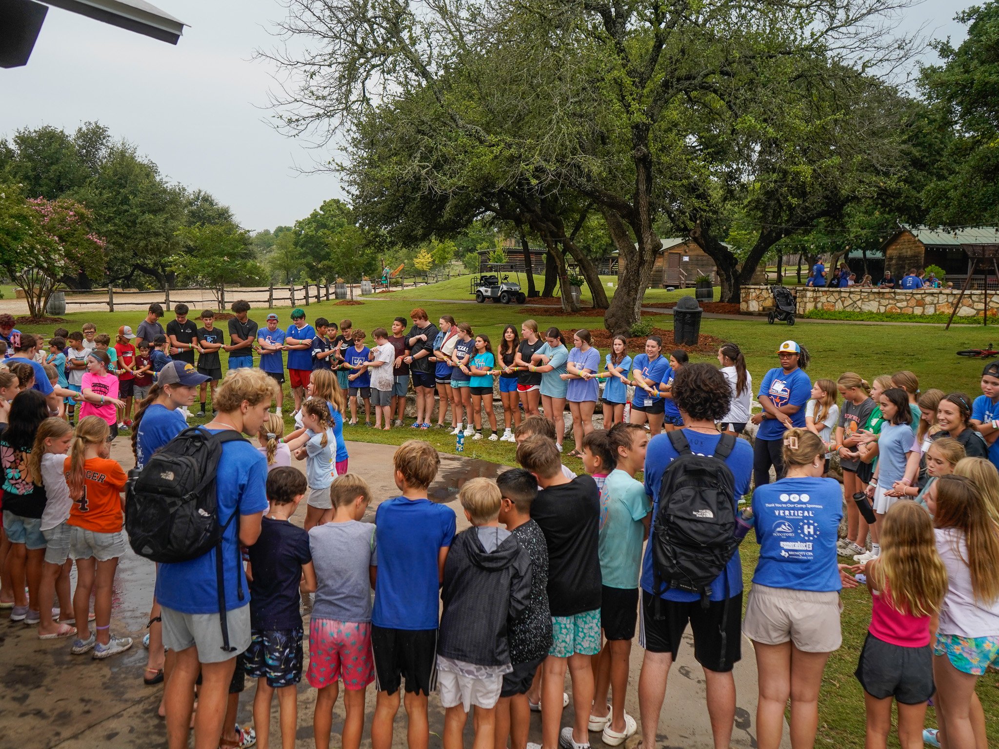 A large group of students gathered in a big prayer circle with arms linked at Christian summer camp