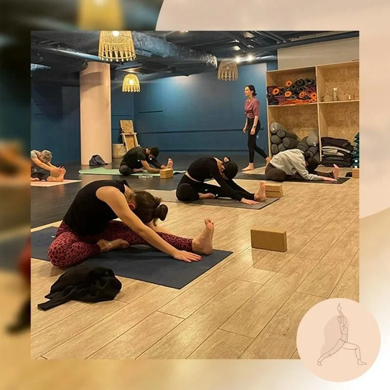 Groupe de personnes participant à un cours de yoga ou de pilates dans une salle intérieure, en position étendue avec une jambe fléchie, utilisant des blocs de soutien.