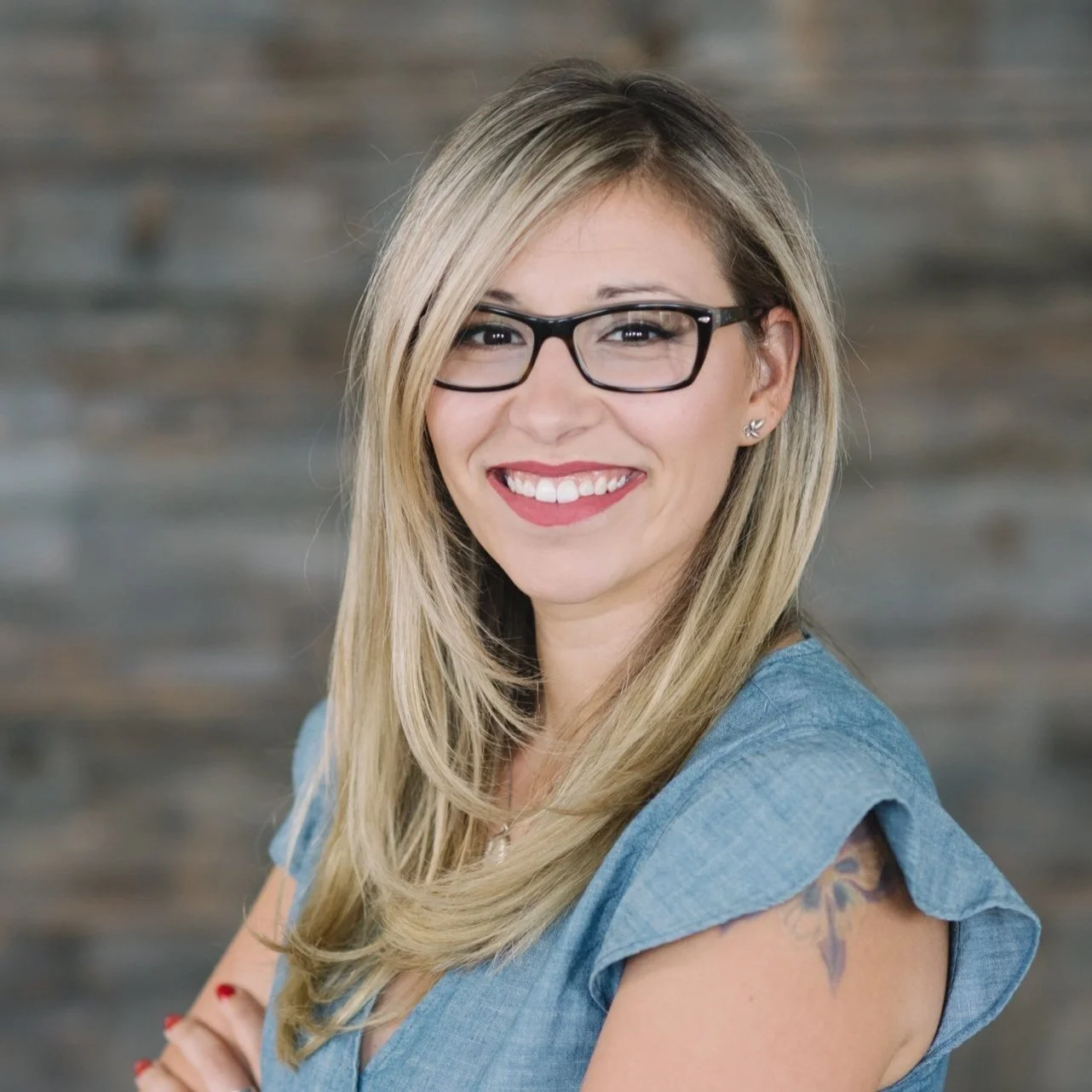 Smiling woman with long blonde hair and glasses, wearing a blue top.