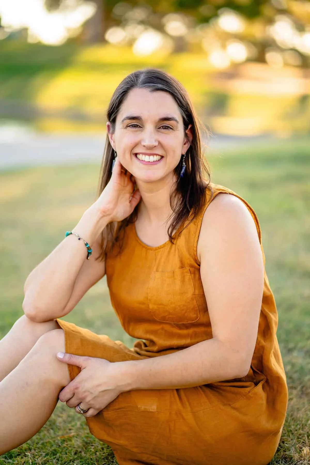 Therapist Tara Nicotra Clemente sitting on grass in yellow dress with blurred sunlight background