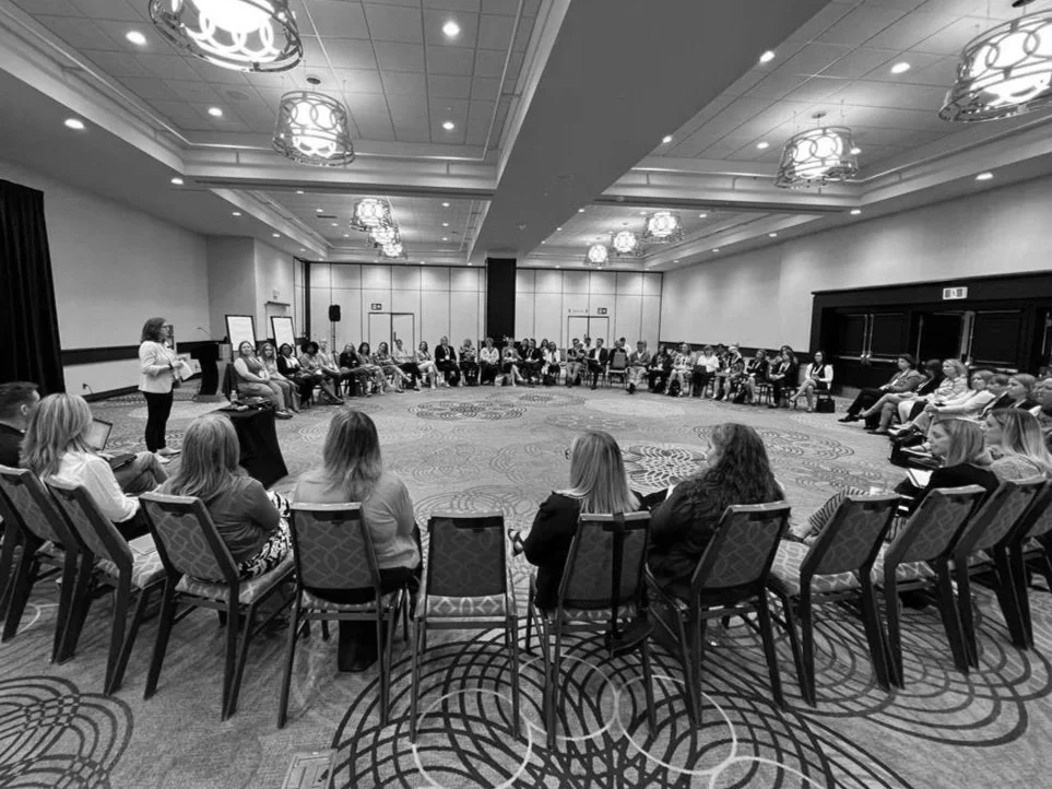 Felicity presenting in front of a group of 70 people seated in a circle. 