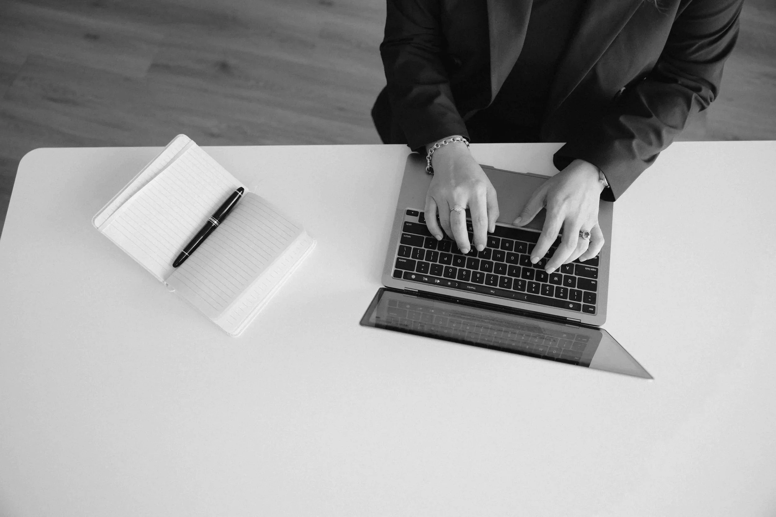 Aerial shot of a laptop and open notebook with a pen.