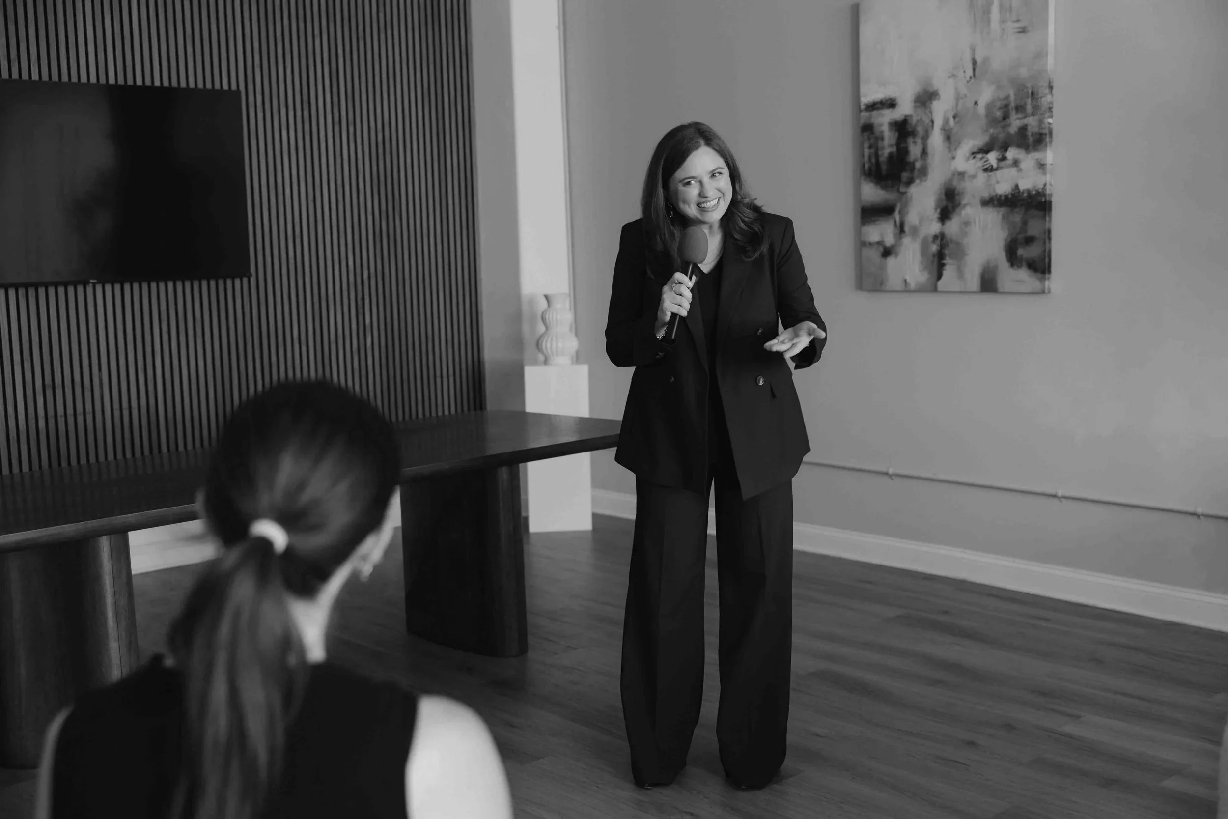 Felicity in a suit speaking into a microphone in front of an audience.