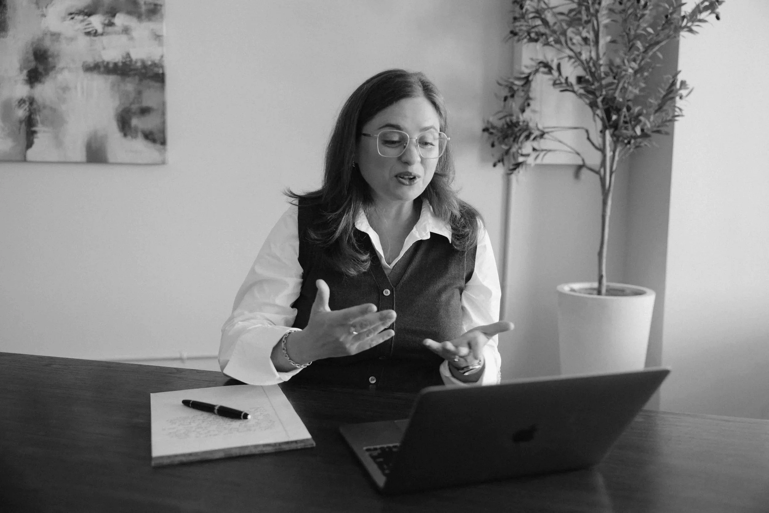 Felicity coaching a client over zoom. She's gesticulating in front of a laptop in an office setting.