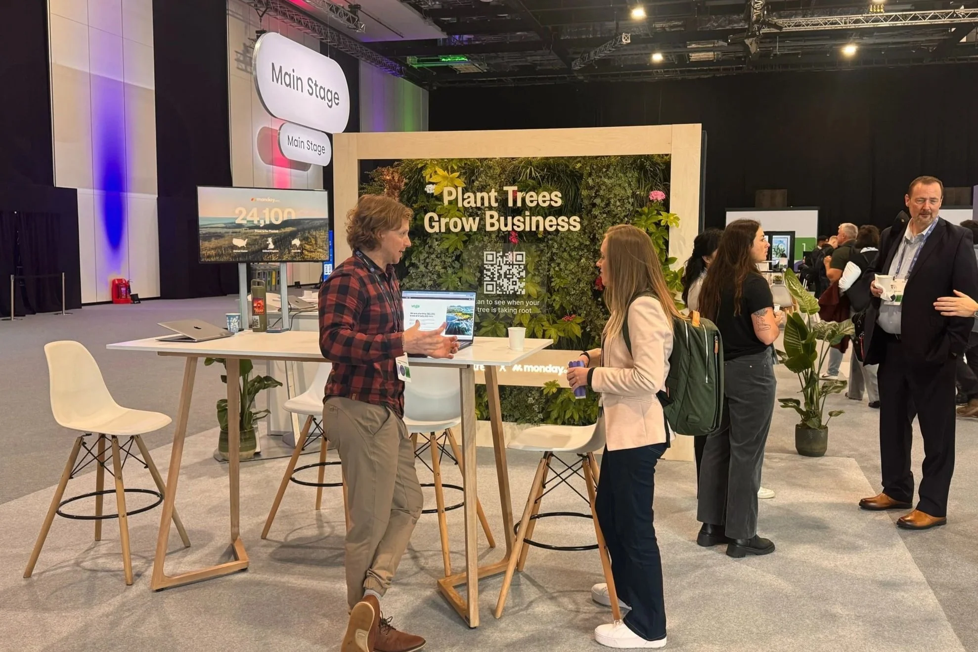 Bespoke sustainable living wall event stand at the Excel, London, with people engaging in conversations at a trade show booth labeled 'Plant Trees Grow Business' .