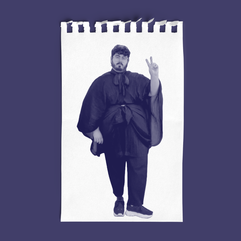 A man with curly hair, glasses, and facial hair standing on a white paper with torn edges. He is wearing dark clothing with a large bow or scarf around his neck and is making a peace sign with his right hand.