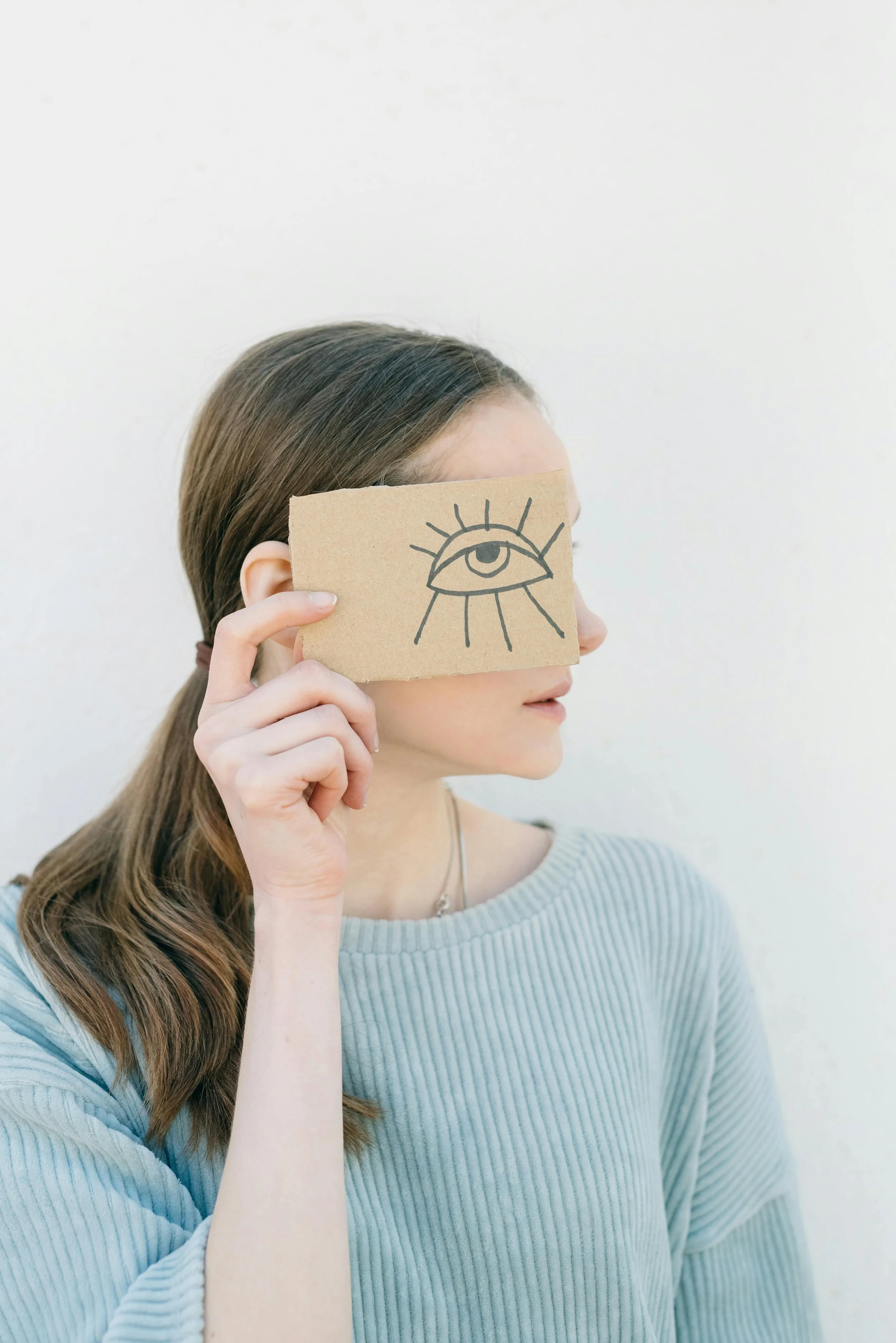 Woman holding a cartoon eye over her face representing the eye movement component of EMDR trauma therapy