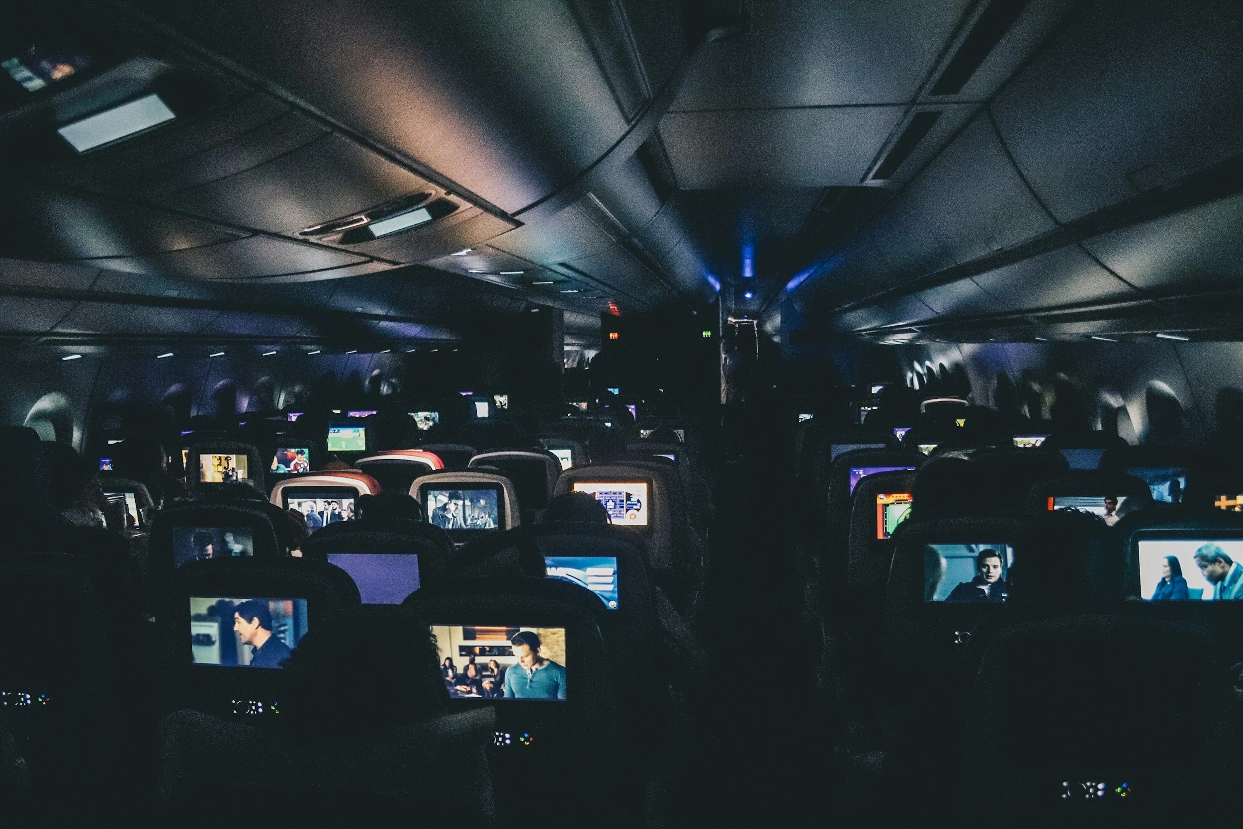 a dark airplane cabin with seatback entertainment displays lit up representing fear of flying treatment with an emdr therapist in san francisco or los angeles