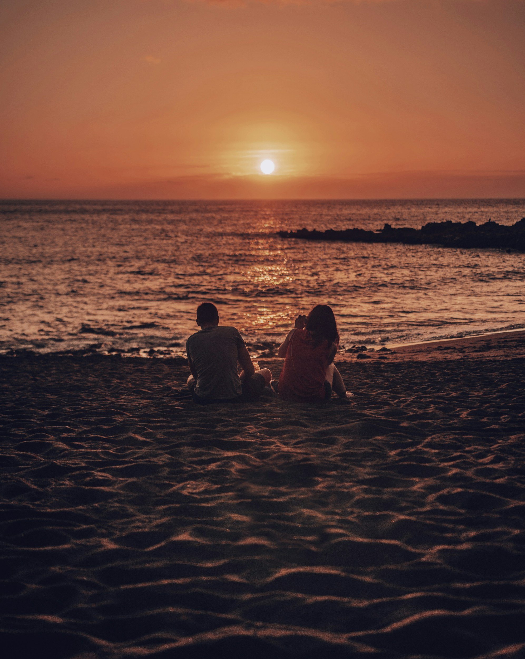Couples sitting on the beach in San Francisco leaning away from each other representing the emotional distance in narcissistic relationship cycles addressed in couples therapy in San Francisco