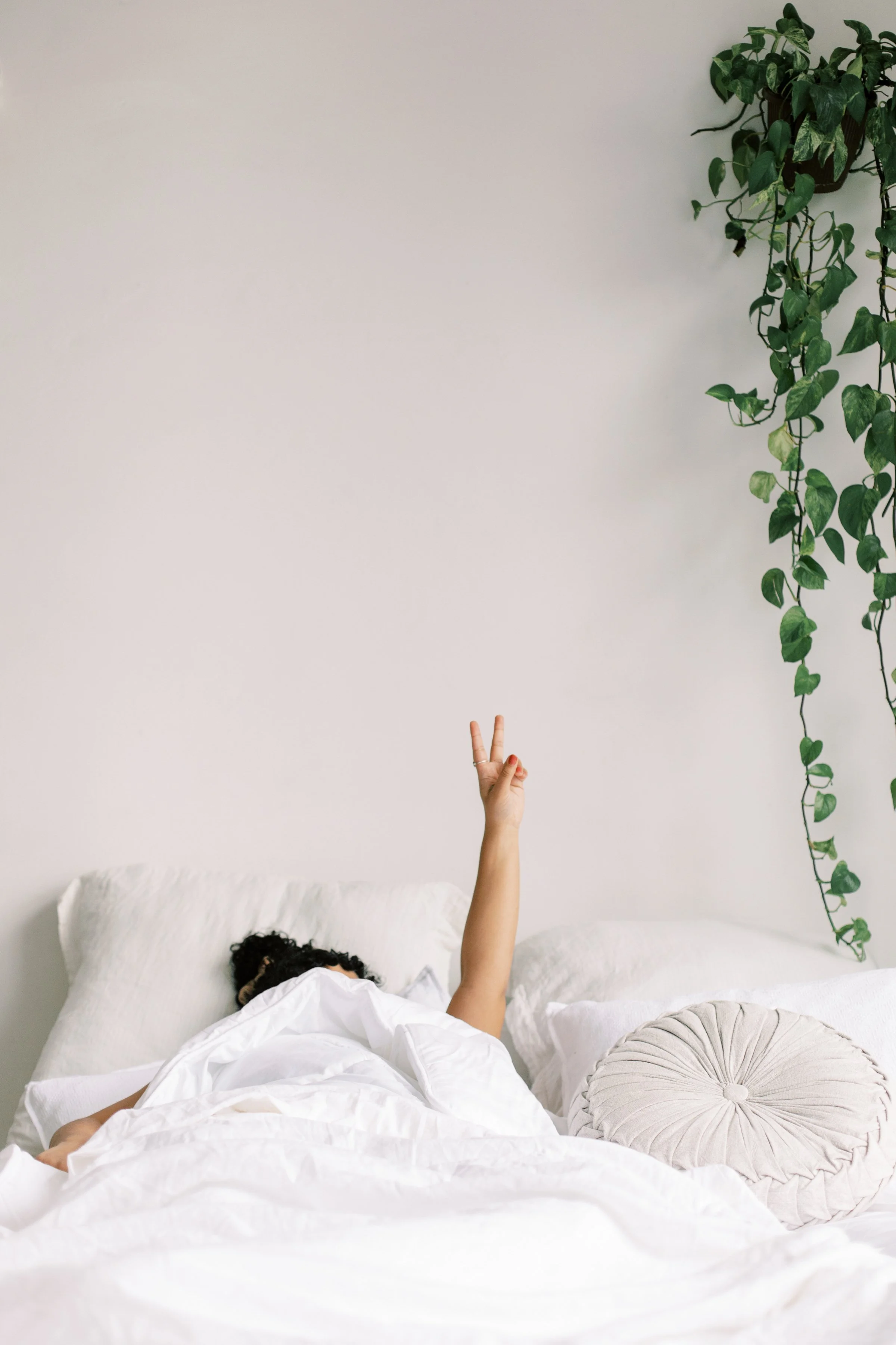 Overwhelmed professional in bed holding up a peace sign, representing burnout therapy in San Francisco