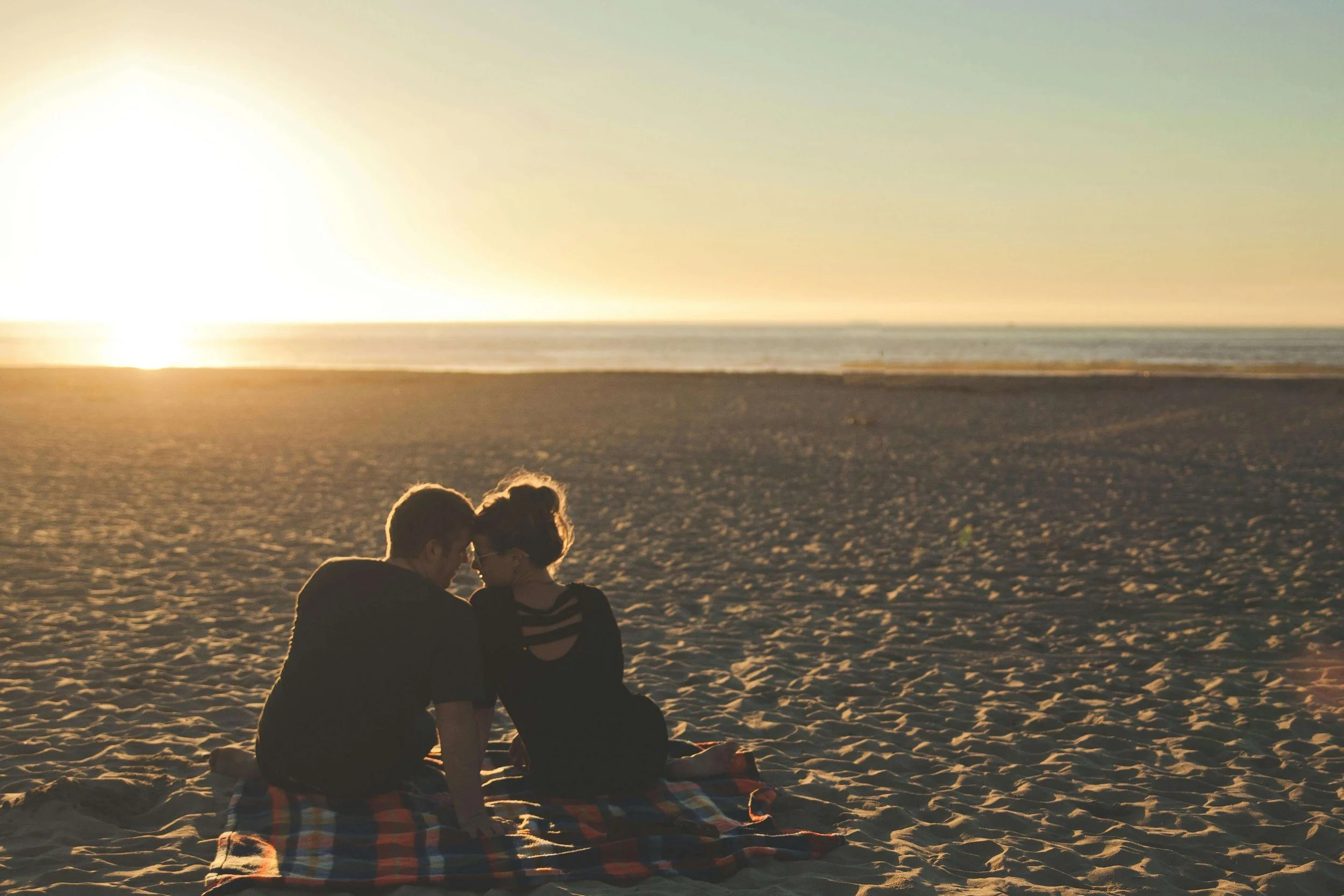 a man and a woman touching foreheads sitting on a blanket on the beach in los angeles representing the result of working with a great couples therapist in los angeles or san francisco
