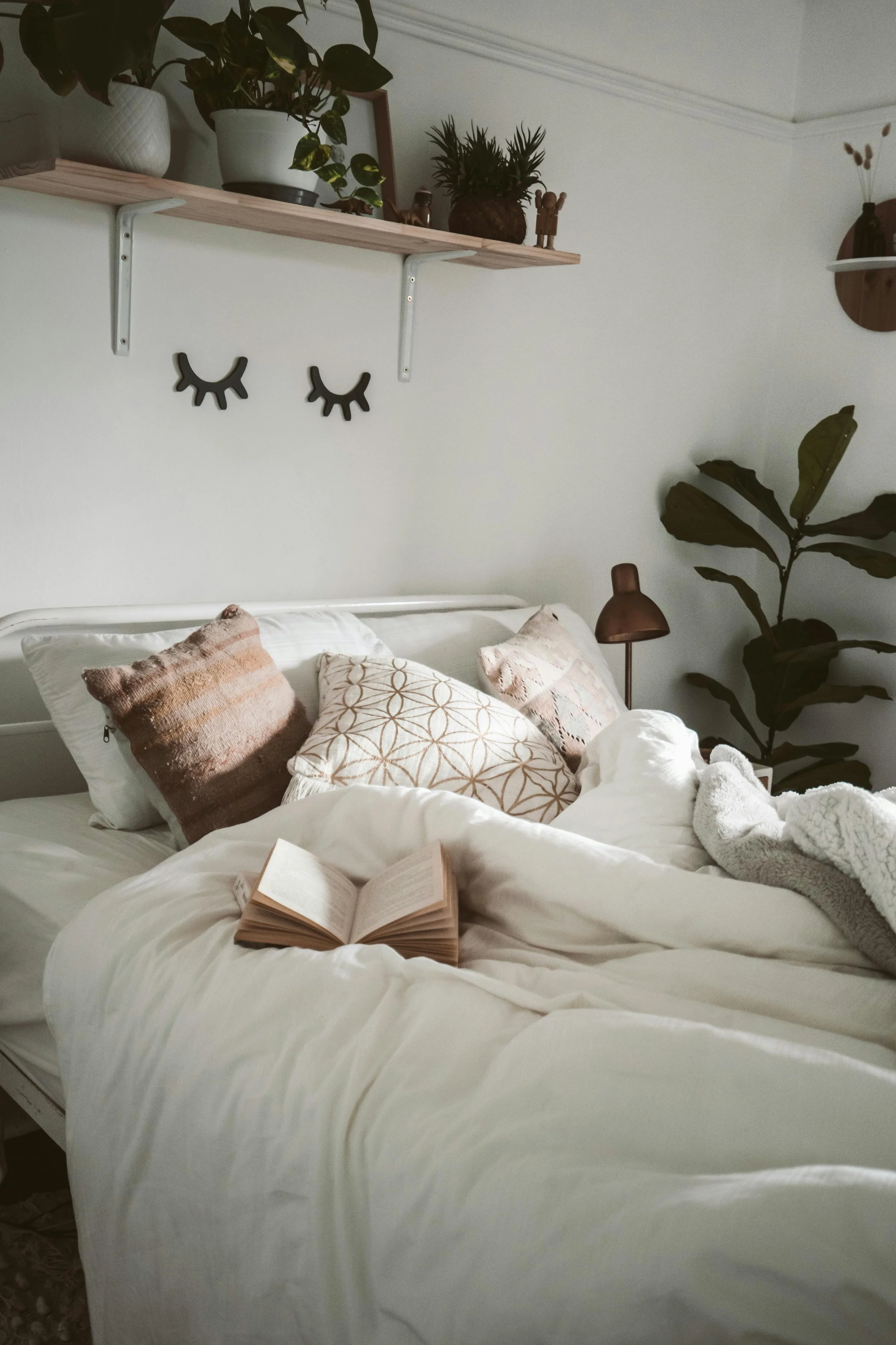 A stylish bed with books, pillows, and plants surrounding it representing JOMO and how holistic therapy can support nervous system regulation