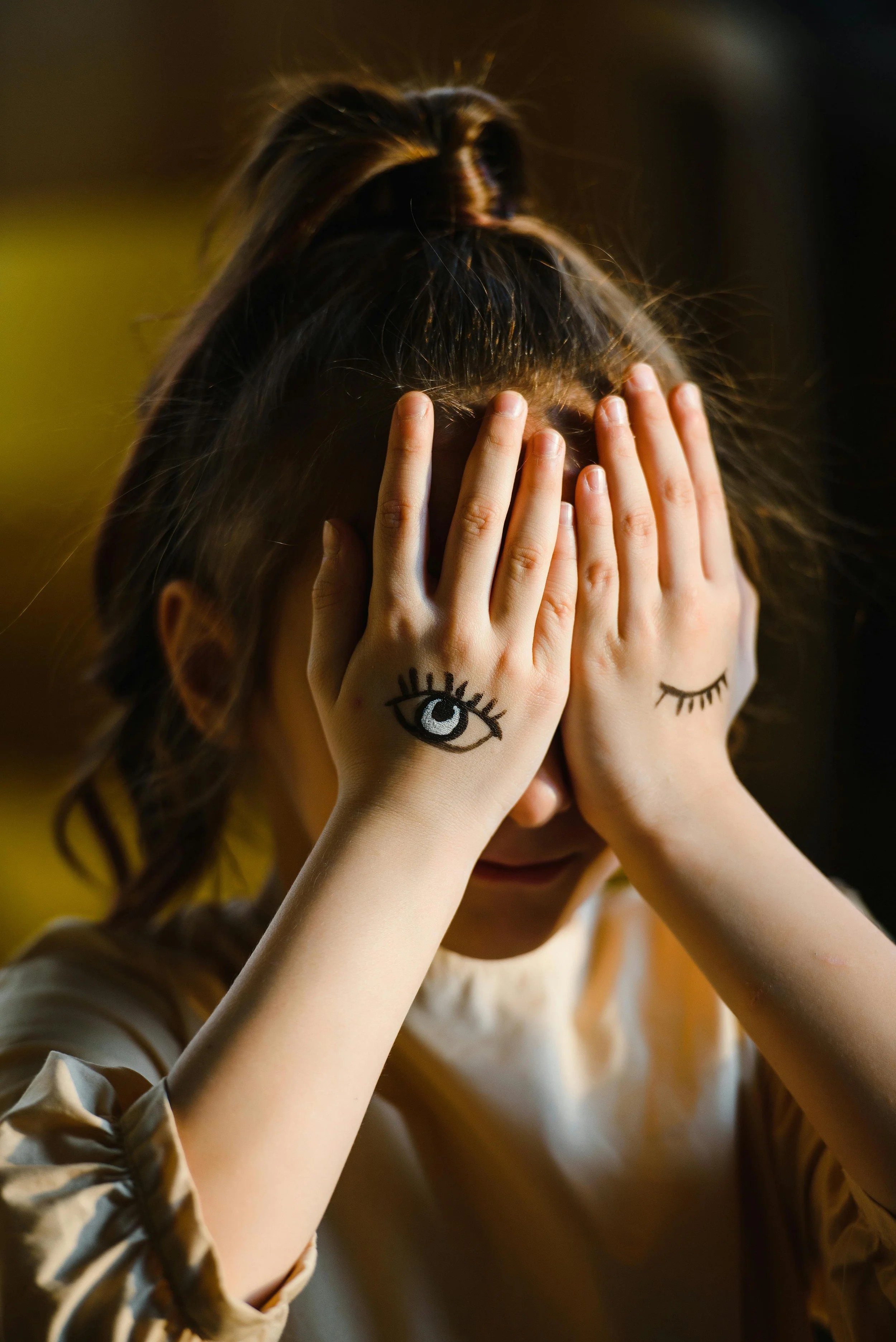 Person covering their face with hands that have eyes painted on them, representing bilateral stimulation in EMDR therapy