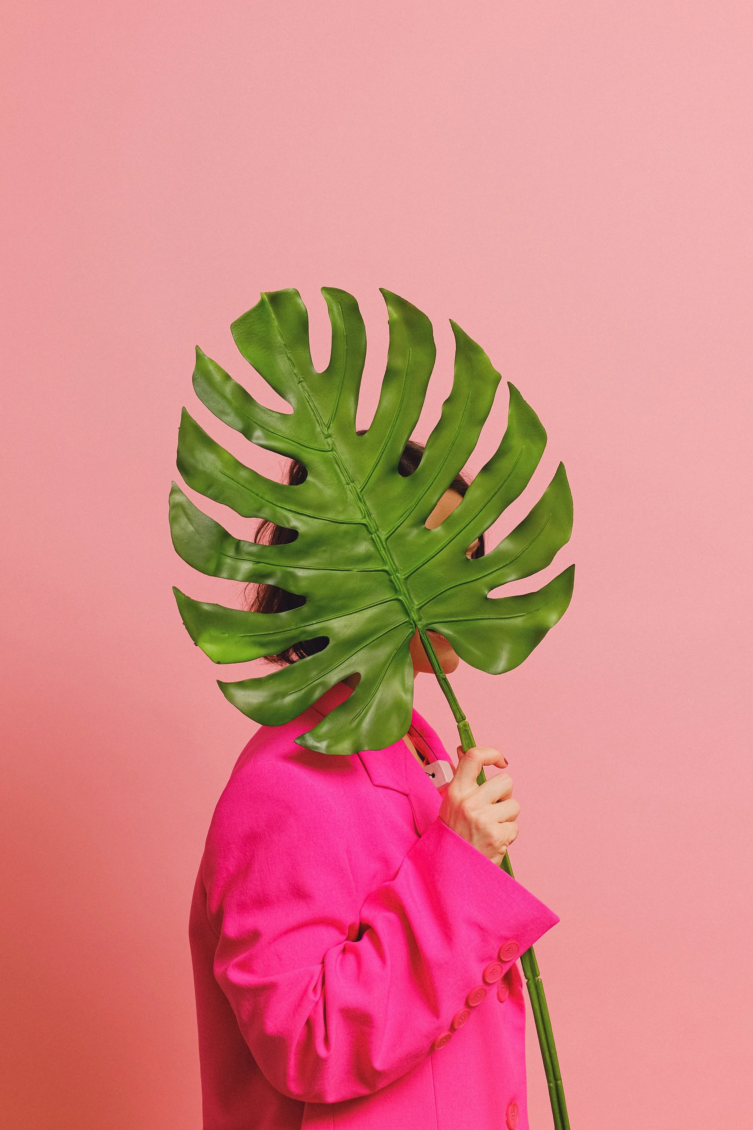 a woman in a hot pink blazer hiding her face behind a monstera leaf representing growth through enneagram therapy in california or florida