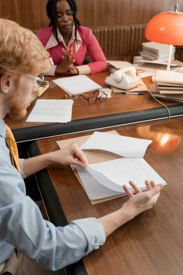Two colleagues sitting at a desk reviewing documents together during a performance evaluation meeting