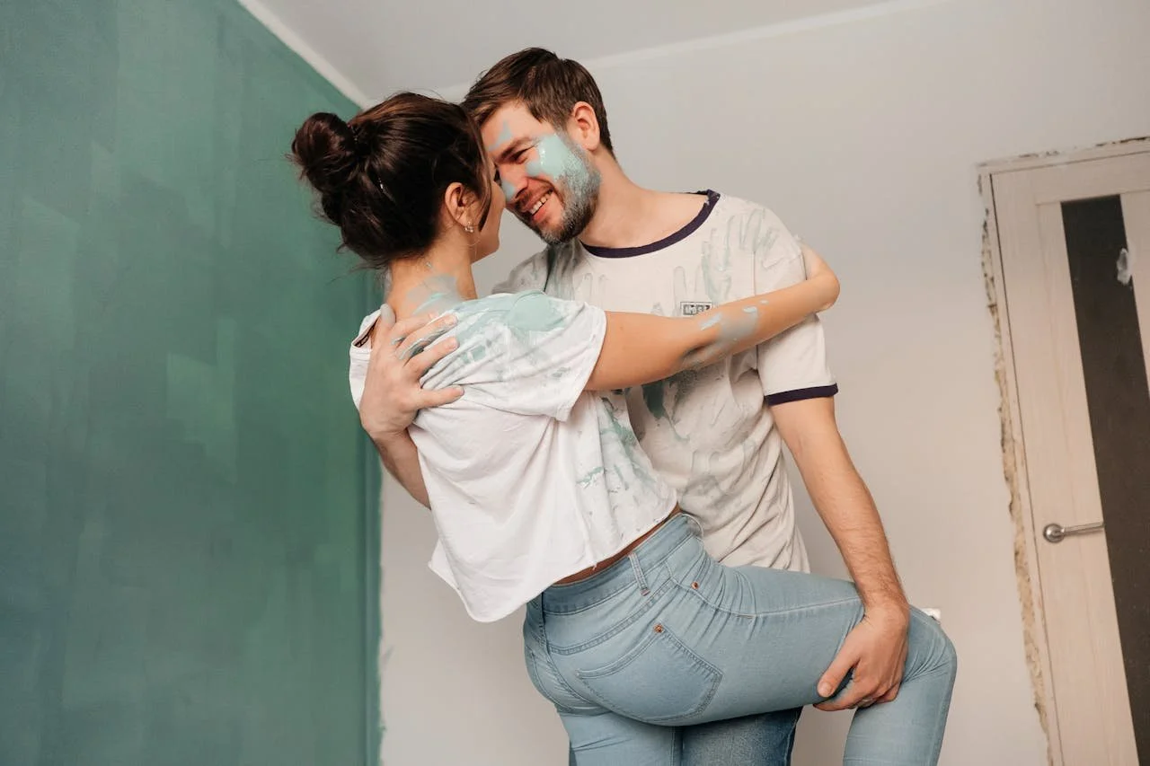 a couple dancing in a freshly painted room with paint on their clothes and faces representing joy through shared meaning, a cornerstone of gottman method couples therapy. our couples therapists are ready to help.