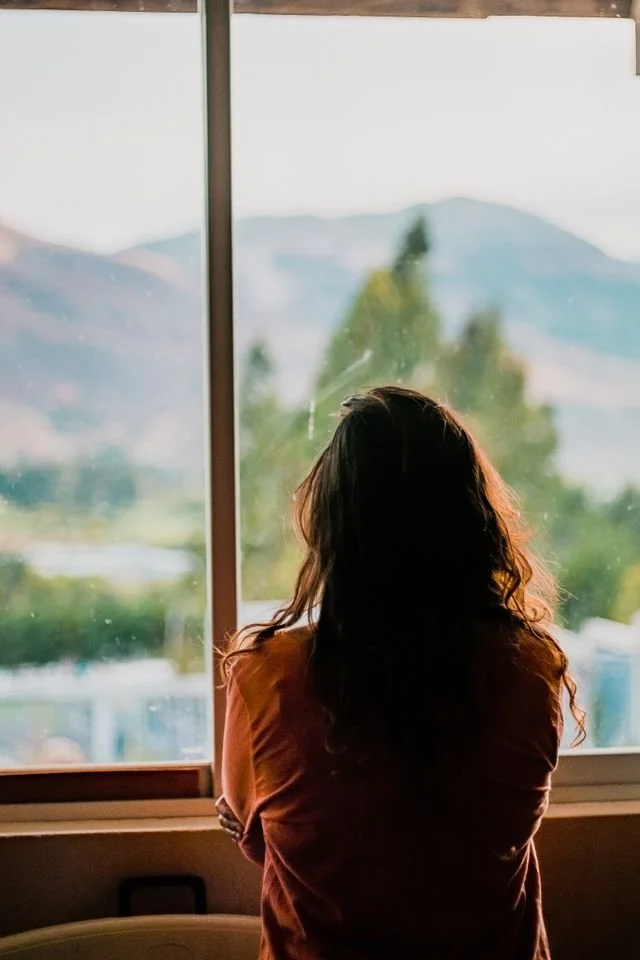 Person looking out a window with an expression of quiet grief representing ontological loss and trauma therapy in Los Angeles