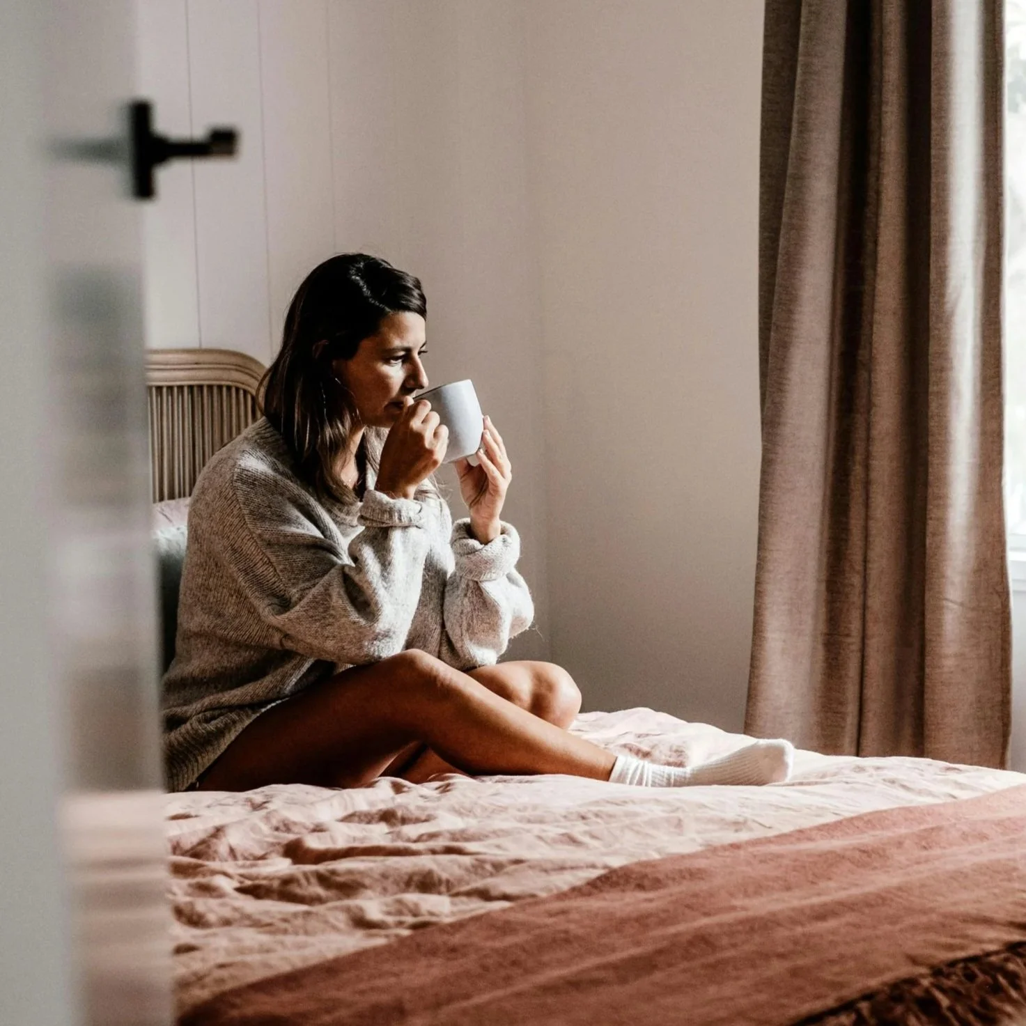 a woman sitting on a bed drinking coffee looking stressed representing someone in need of emdr therapy in san francisco or los angeles