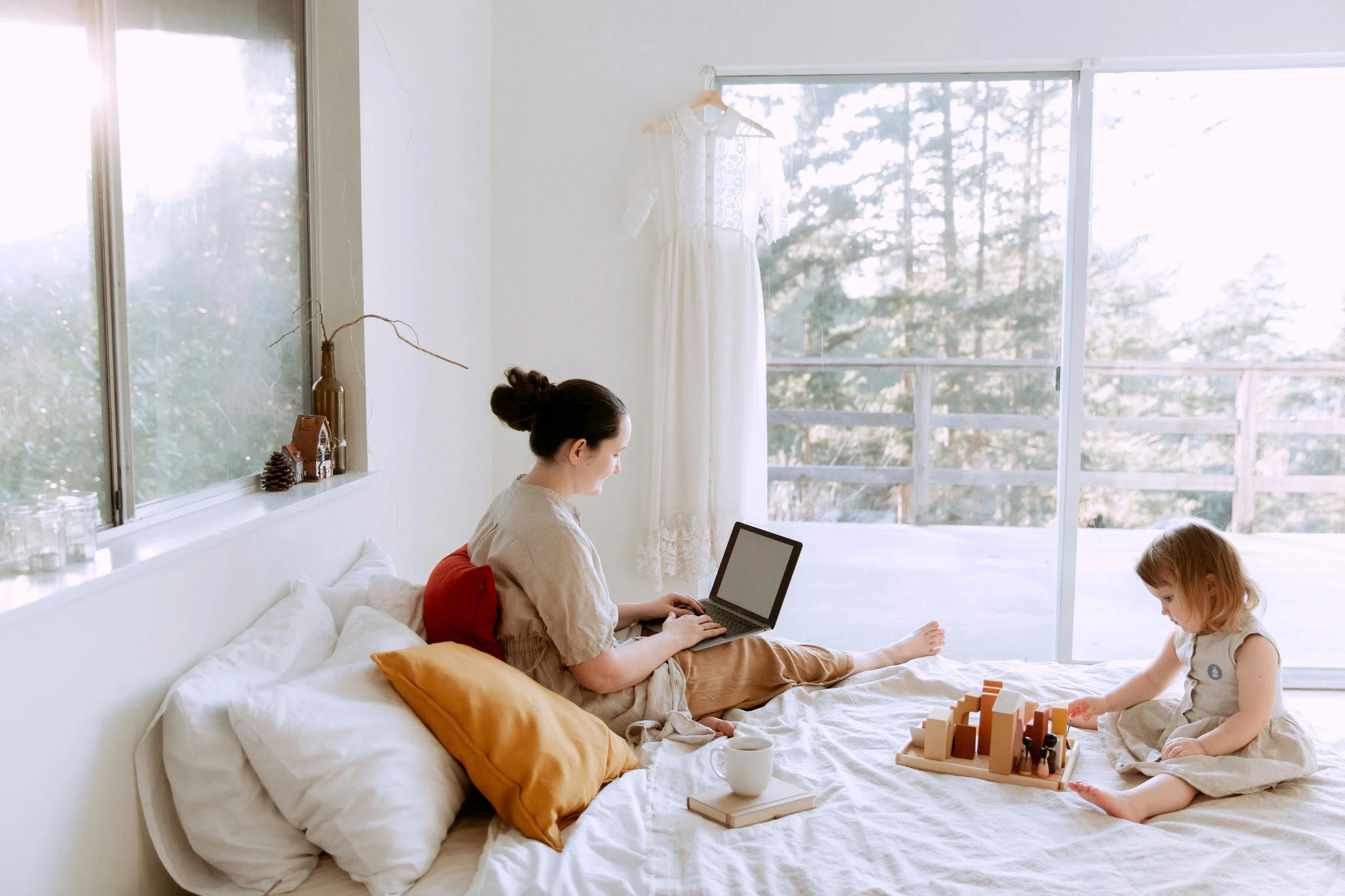 Person calmly working on their laptop in bed while their toddler plays quietly representing intentional rest and holistic therapy in San Francisco