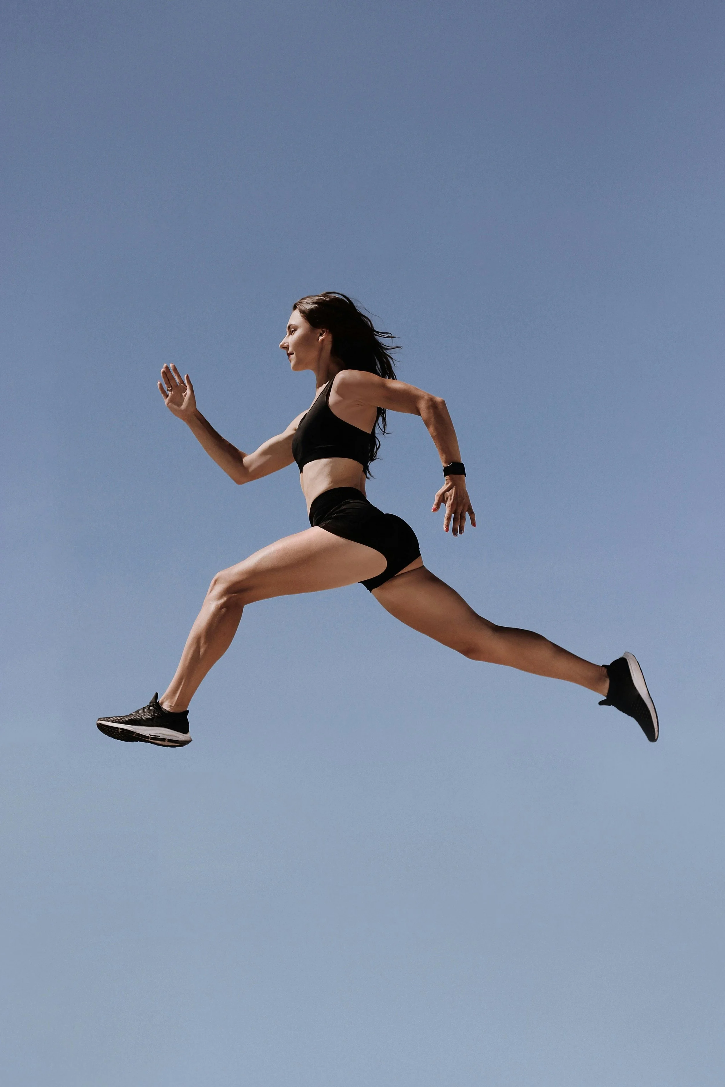 a woman in black athletic gear leaping high into the air against a blue sky representing resilience gained through trauma therapy and emdr therapy in los angeles