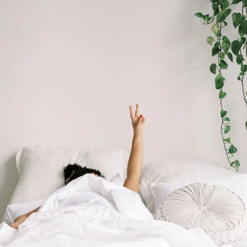 Overwhelmed professional in bed holding up a peace sign, representing burnout therapy in Santa Cruz