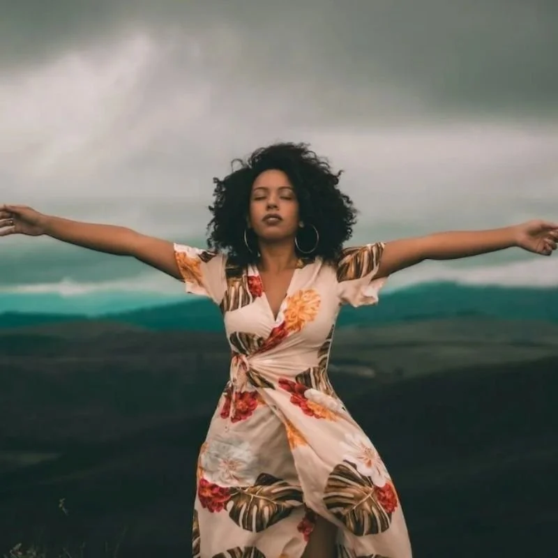 a woman with dark curly hair with her arms outstretched in front of a cloudy ocean landscape representing someone who has overcome rape or sexual assault through EMDR therapy los angeles