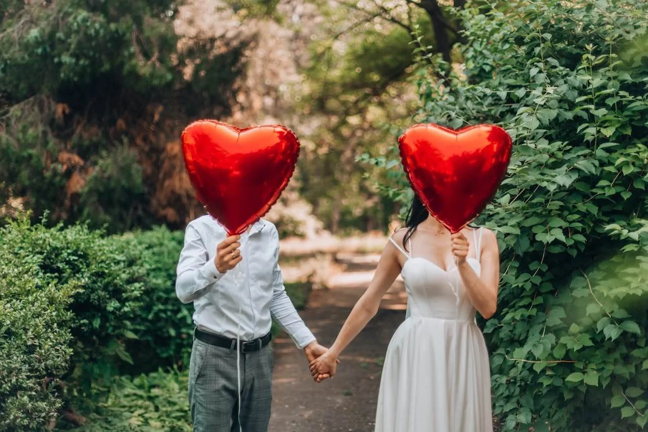 two people holding hands with red mylar balloons held in front of their heads representing healthy love and steady relationship pacing through work with a great couples therapist in los angeles or san francisco