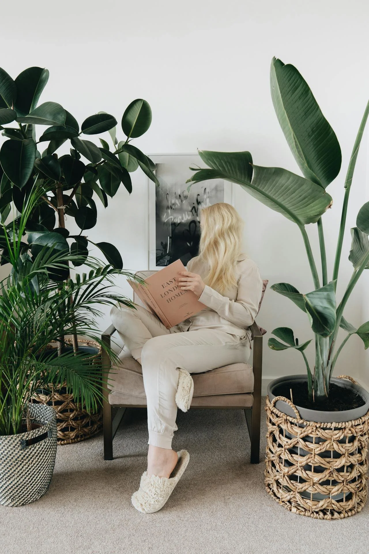 Person resting reading a book between multiple large houseplants representing genuine nervous system recovery and burnout healing in California